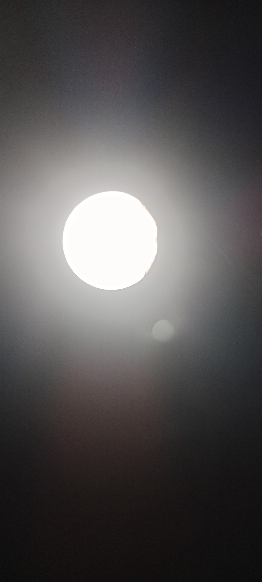 A lightbulb is illuminated against a dark background. There are some subtle color shifts in the background, suggesting ambient light. The image's composition is centered on the lightbulb, with the surrounding darkness creating a stark contrast. The scene is devoid of any environmental context that would indicate a specific location within Pelang, Indonesia, or any other geographical area. There are no individuals or discernible objects present other than the lightbulb.