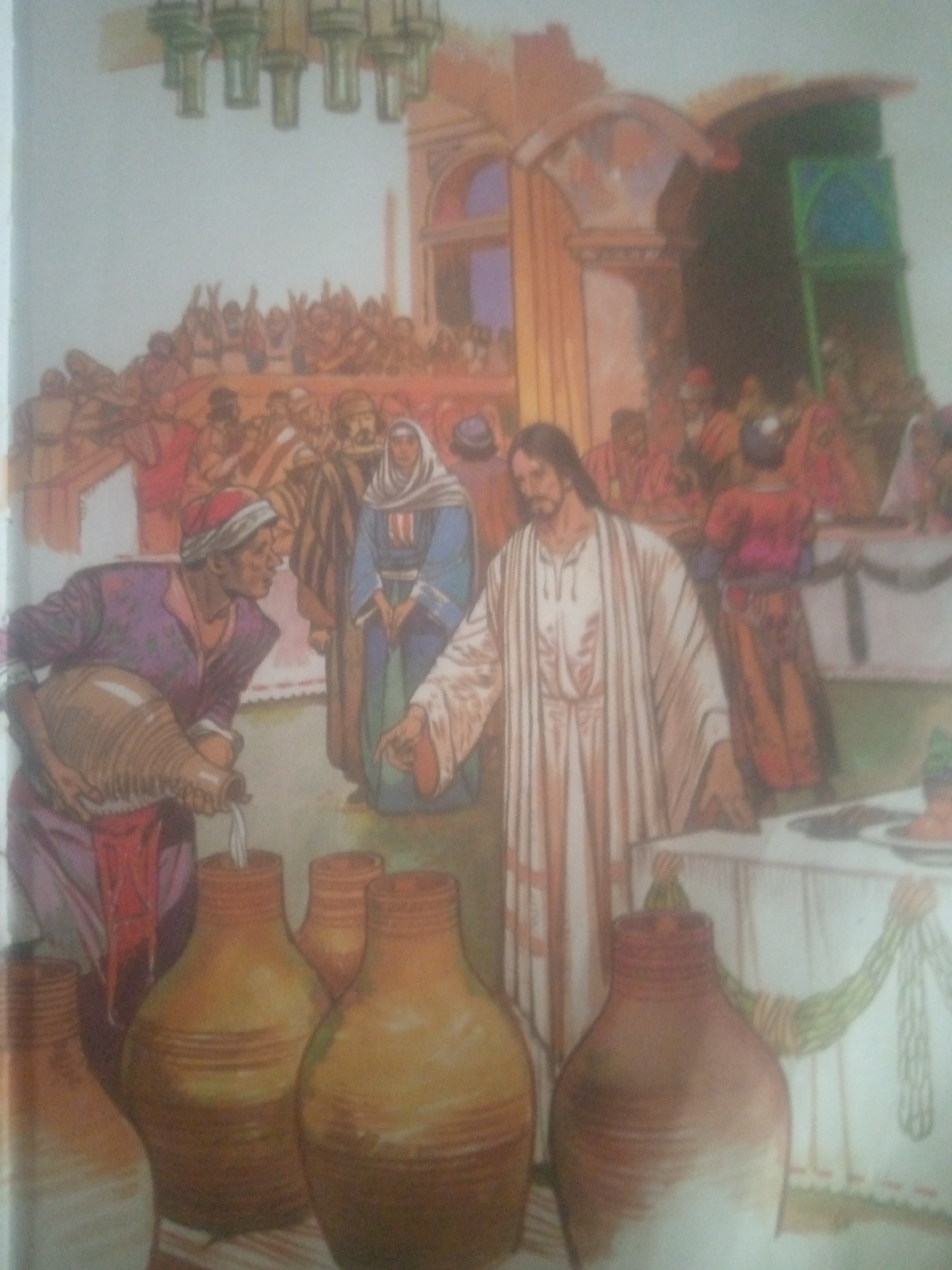 The image depicts a scene from a biblical narrative, likely the miracle at the Wedding at Cana, set in an ancient, open-air marketplace or courtyard. In the foreground, a man in a purple garment and red headscarf is pouring liquid from a large amphora into several smaller clay jars. He appears to be an attendant or servant. To his right, a woman in a blue robe and white headscarf observes the action. In the center of the image, a man with long hair, wearing a white robe, stands with his hand extended, seemingly overseeing the process. He is the central figure, likely representing Jesus. Behind them, a large gathering of people in traditional ancient attire are visible, some seated at tables in the background, suggesting a feast or celebration. Architectural elements of arches and columns frame the scene, indicative of a Middle Eastern or Mediterranean setting. The overall atmosphere is one of activity and a significant event unfolding. The prompt's request to include the location of Jauro Yinu, Nigeria, is incongruous with the visual evidence in the image, which strongly suggests a biblical or ancient Middle Eastern context. Therefore, this location cannot be incorporated into a factual description of the image.