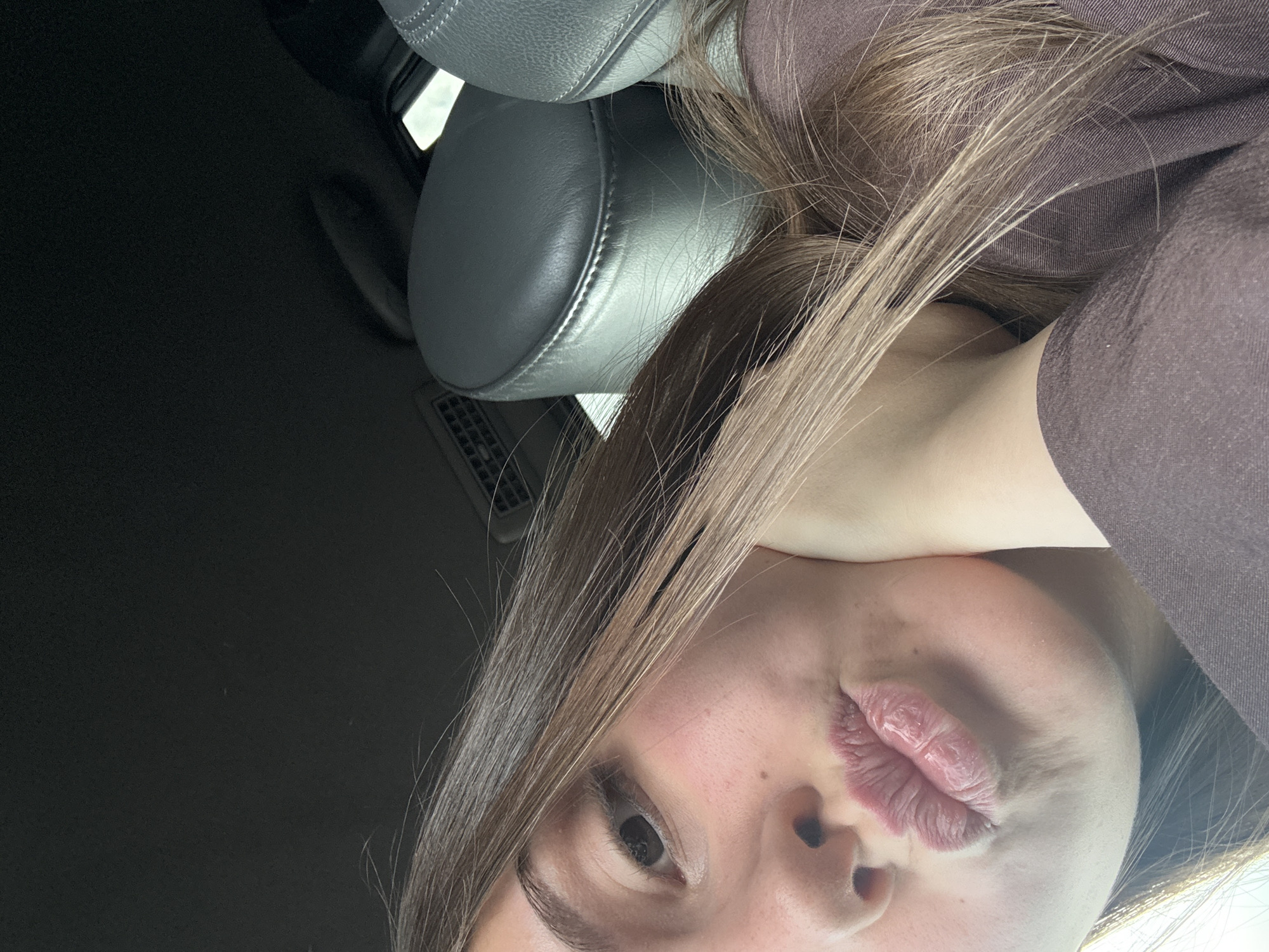 A close-up selfie depicts a fair-skinned individual with brown hair and a pursed mouth. The person is wearing a brown top. The background shows the interior of a car, with a gray headrest visible. The exact location within Burgas, Bulgaria cannot be determined from the image.