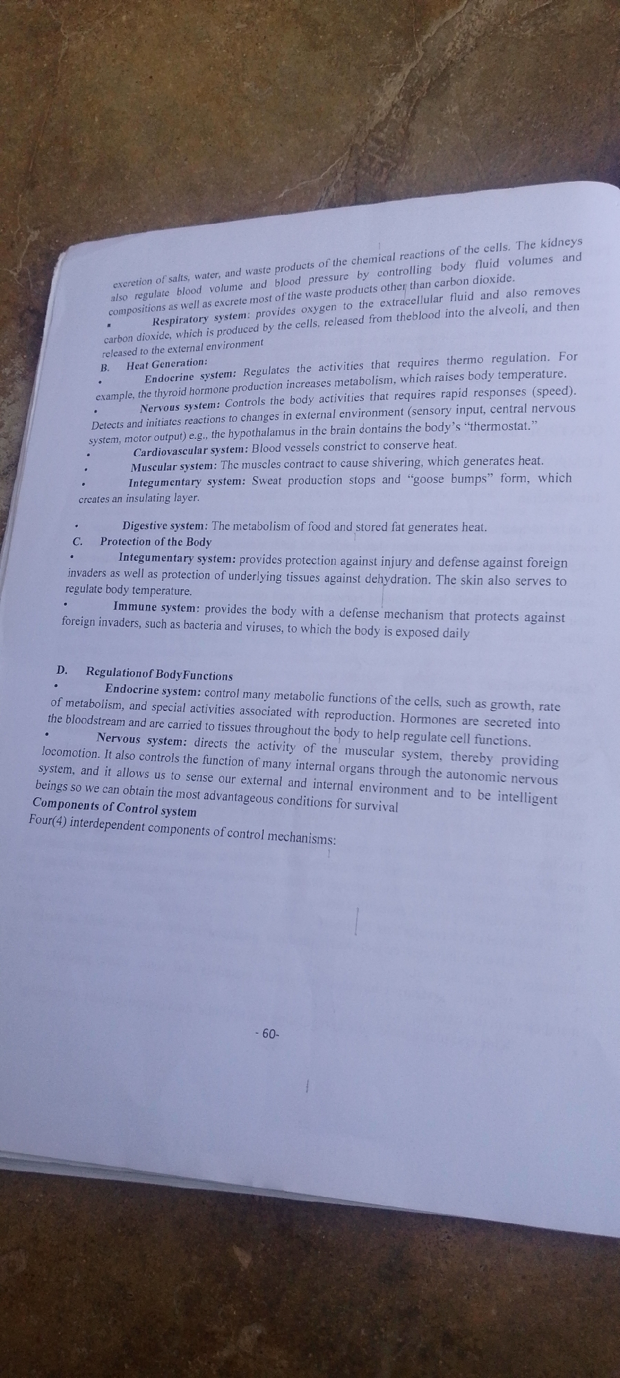 The image shows a close-up, slightly angled, overhead view of a page from a textbook or manual. The text is printed in black ink on white paper. The page appears to be from a biology or human anatomy and physiology section, as evidenced by the headings and descriptions of various body systems such as the respiratory system, endocrine system, nervous system, cardiovascular system, muscular system, integumentary system, digestive system, and immune system. The text also discusses concepts like heat generation, protection of the body, and regulation of body functions. Some bullet points are used to list specific systems and their functions. In the bottom right corner of the page, there is a page number "-60-". The background of the image is a textured surface, possibly a table or desk, with a marbled or speckled pattern in shades of brown and beige. The lighting suggests an indoor setting, and there are no visible people or external environmental elements like weather or cityscapes.