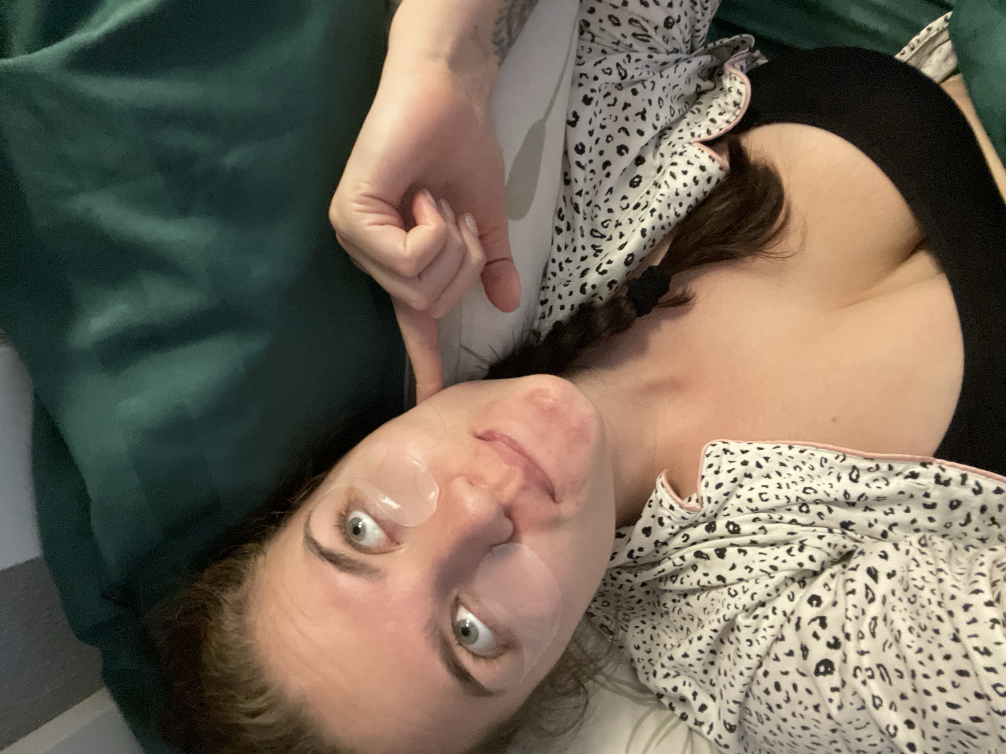 A person is lying down, possibly on a bed, with a green pillow visible in the top left corner. They are wearing eye masks and have a black top and a leopard print pajama top. Their left hand is raised near their face. A single braid is visible on their chest. The location in the city of Мосметаллоконструкция Онт, Russia, is not directly discernible from the image.