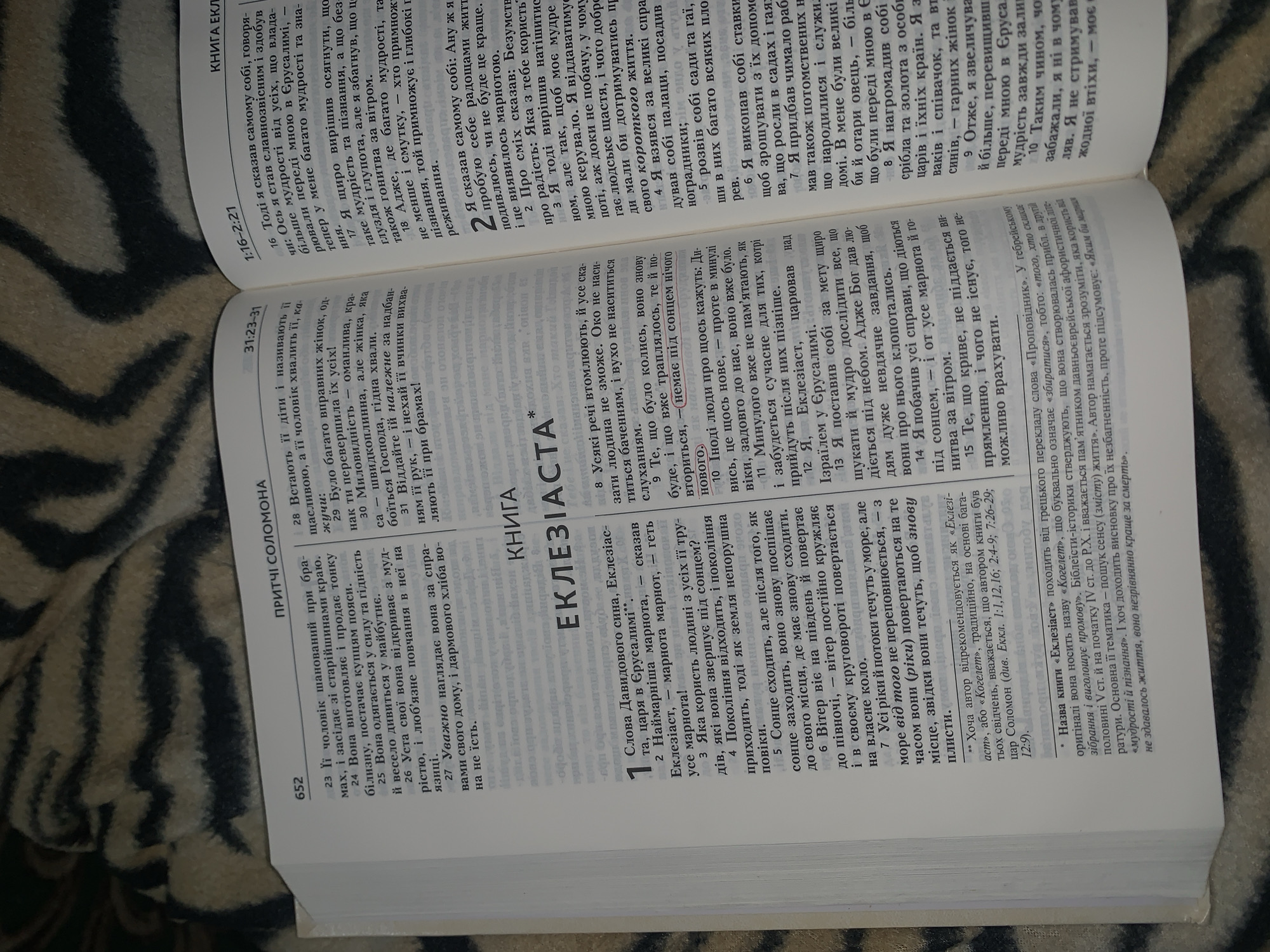 This is a close-up, top-down, indoor shot of an open book, likely a Bible, resting on a dark, textured surface. The book is open to two pages of text. The left page contains a heading "ПРІТЧІ СОЛОМОНА" and text in Ukrainian, with numbered verses. The right page has a heading "КНИГА ЕКЛ" and text in Ukrainian, also with numbered verses. The lighting is dim, creating shadows and highlighting the texture of the book's pages and the surface it lies on. There are no people or any indication of location in Nekrashi, Ukraine.
