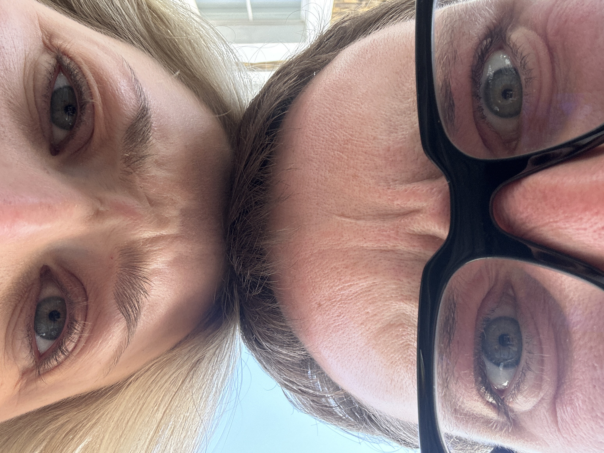 The image shows two faces from a low, upward angle. On the left is a person with blond hair, fair skin, and light eyes. On the right is another person with brown hair, fair skin, light eyes, and glasses with black frames. The foreheads are close together in the center of the image. The background is light blue, possibly the sky. There is no indication of the city of London.