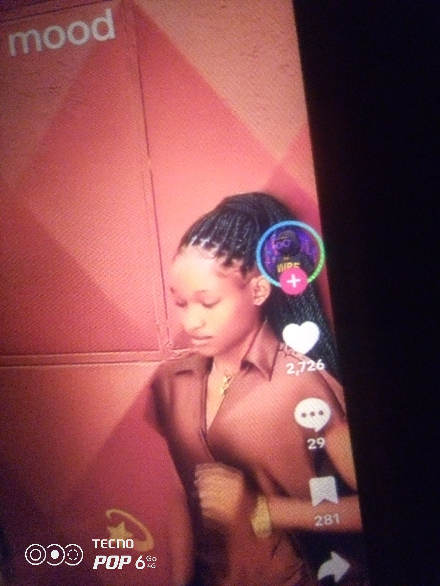 The image shows a young woman with braided hair wearing a brown top. She is standing in front of a pink textured wall. There are social media icons and engagement metrics visible on the right side of the image, including a heart with "2,726" likes, a speech bubble with "29" comments, and a bookmark icon with "281" saves. The word "mood" is visible in white text on the upper left of the wall. A Tecno Pop 6 4G logo is present in the lower left corner of the image. The background is dark on the right side. The scene does not provide any specific information about the city of Howayi, Nigeria.