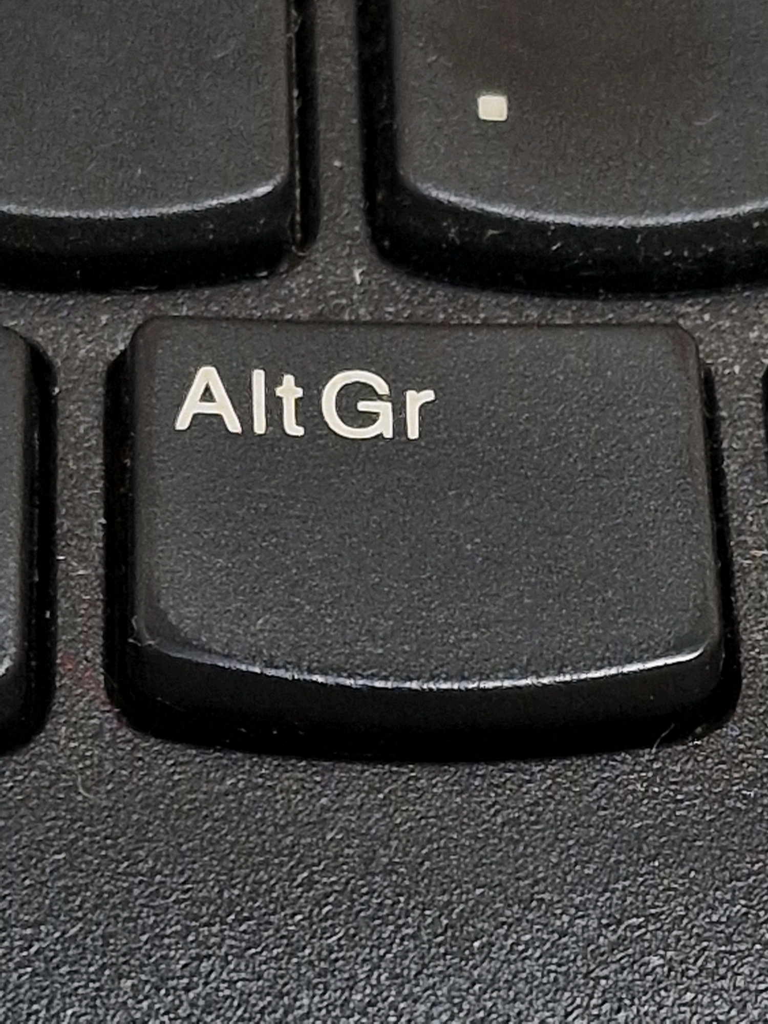 A close-up, eye-level, vertical shot focuses on a black computer keyboard. The "Alt Gr" key is centrally located and in sharp focus, with its white text clearly legible. To the left and right of this key are other black keys, partially visible and out of focus. The textured surface of the keyboard is visible beneath the keys. The image does not contain any information about Travnik, Bosnia and Herzegovina, people, actions, or interactions.