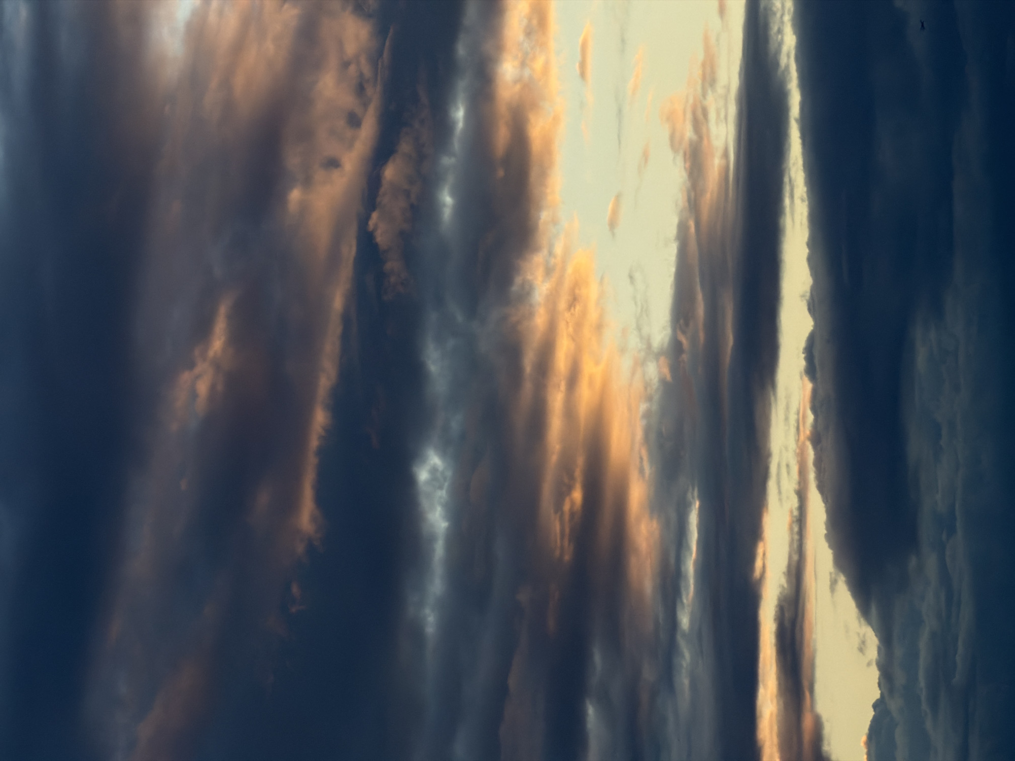 The image depicts a sky filled with dark, heavy clouds. The clouds are illuminated with streaks of orange and gold light, suggesting either sunrise or sunset. The overall mood is dramatic and potentially stormy. No people or objects are discernible in the image. The city and location are unknown.