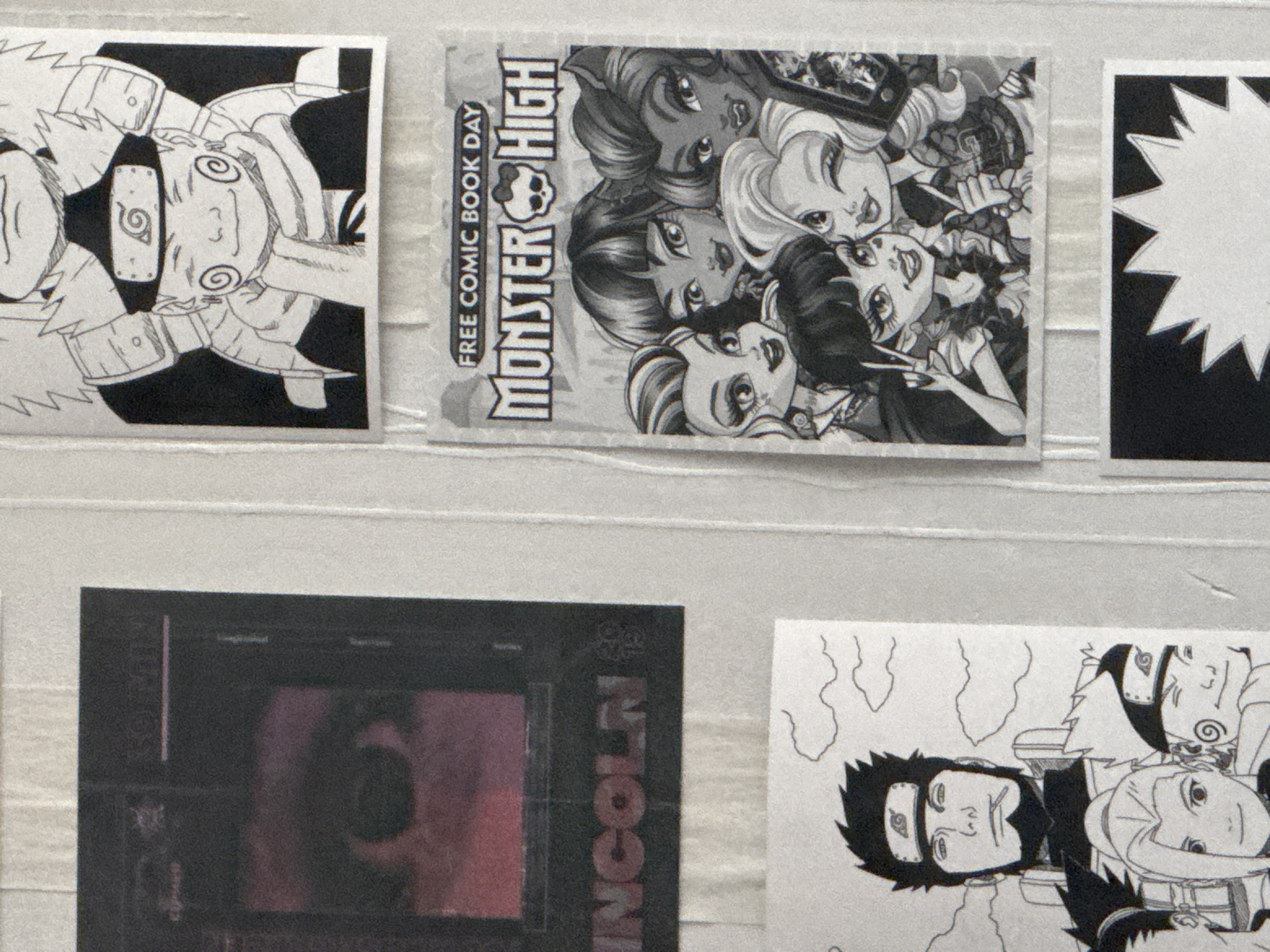 The image is a close-up, slightly blurry photograph of a wall with several posters or prints taped to it. The posters are arranged vertically and horizontally.
In the upper left quadrant, there is a poster with a dark background featuring a close-up of a human eye with a purple hue, and text that appears to read "LINCOLN".
To the right of the "LINCOLN" poster, and occupying the upper right quadrant, is a black and white drawing of characters from the anime series "Naruto". The prominent figure is a child character with spiky hair and a scarf. Below this "Naruto" drawing is a smaller print for "FREE COMIC BOOK DAY" featuring characters from "Monster High" in a stylized, animated manner.
In the lower left quadrant, there is another black and white drawing of "Naruto" characters, including a man with a beard and headband, and other younger characters.
In the bottom center, there is a black poster with a white starburst graphic.
The wall itself appears to be made of vertical panels, possibly a partition or a wall with a textured finish. There are faint horizontal lines across the top of the image, suggesting the edge of another panel or a light source. The overall impression is of a collage of various popular culture references, possibly displayed in a bedroom or a fan's personal space. The lighting is somewhat harsh, creating shadows and reducing the clarity of the details. There is no indication of the location in Moscow, Russia, or any specific urban environment.