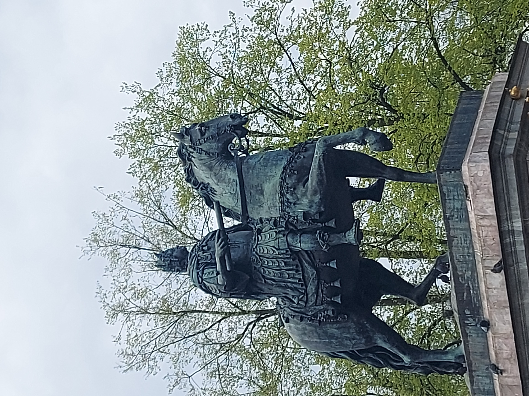 The image shows a bronze equestrian statue of Nicholas I in Saint Petersburg, Russia, situated on a pedestal with trees and sky in the background. The statue depicts Nicholas I in military attire, mounted on a rearing horse.