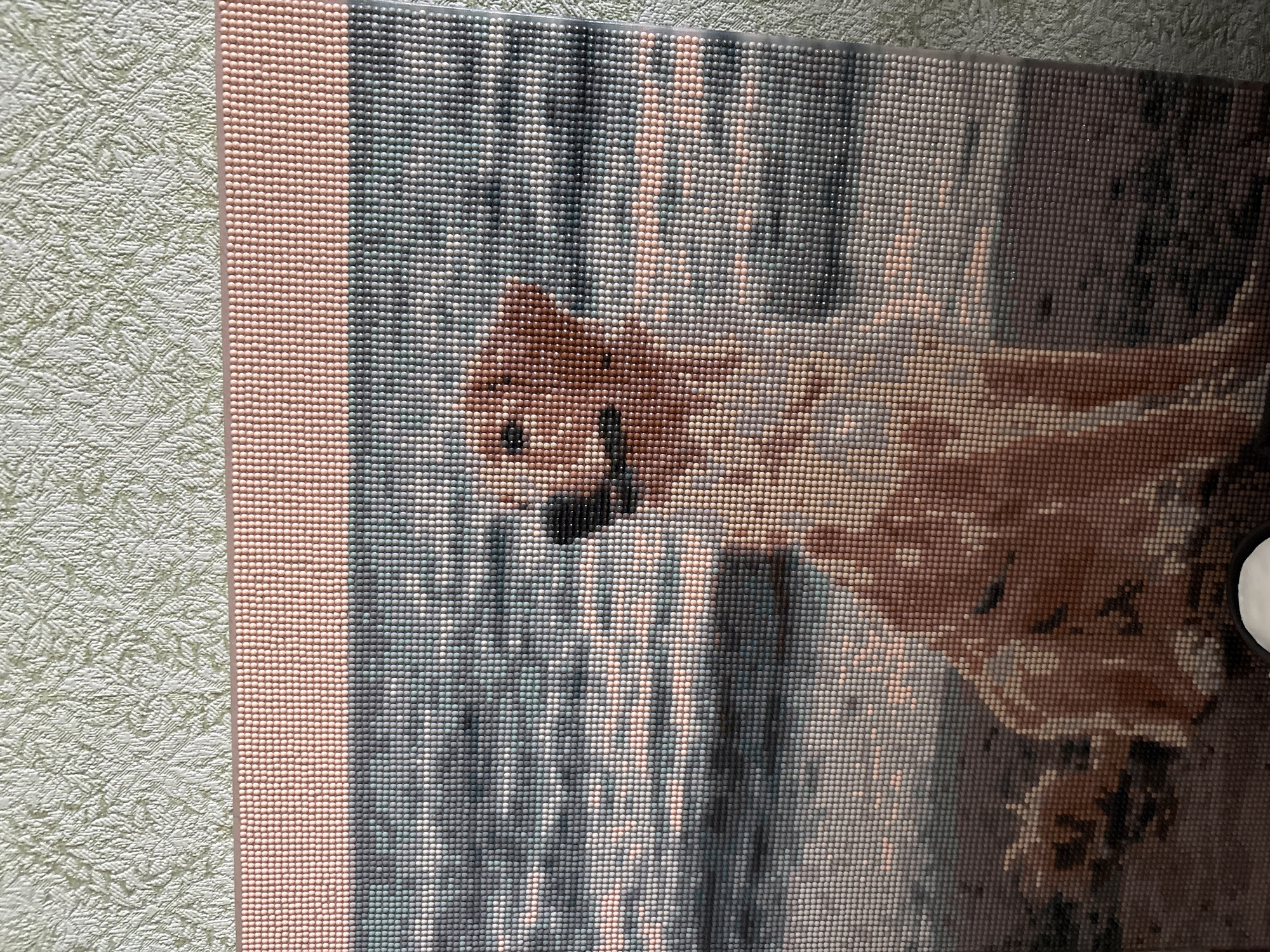 This is a diamond painting of a Golden Retriever sitting on a beach. The dog is facing left, with its head turned towards the viewer. The water is in the background, with ripples and reflections of the sky. The sand is light brown, and there are some rocks and seaweed in the foreground. The diamond painting is framed by a pink border at the top and a textured green wallpaper is visible in the background. There is no information about the location in the city of Rezh, Russia.