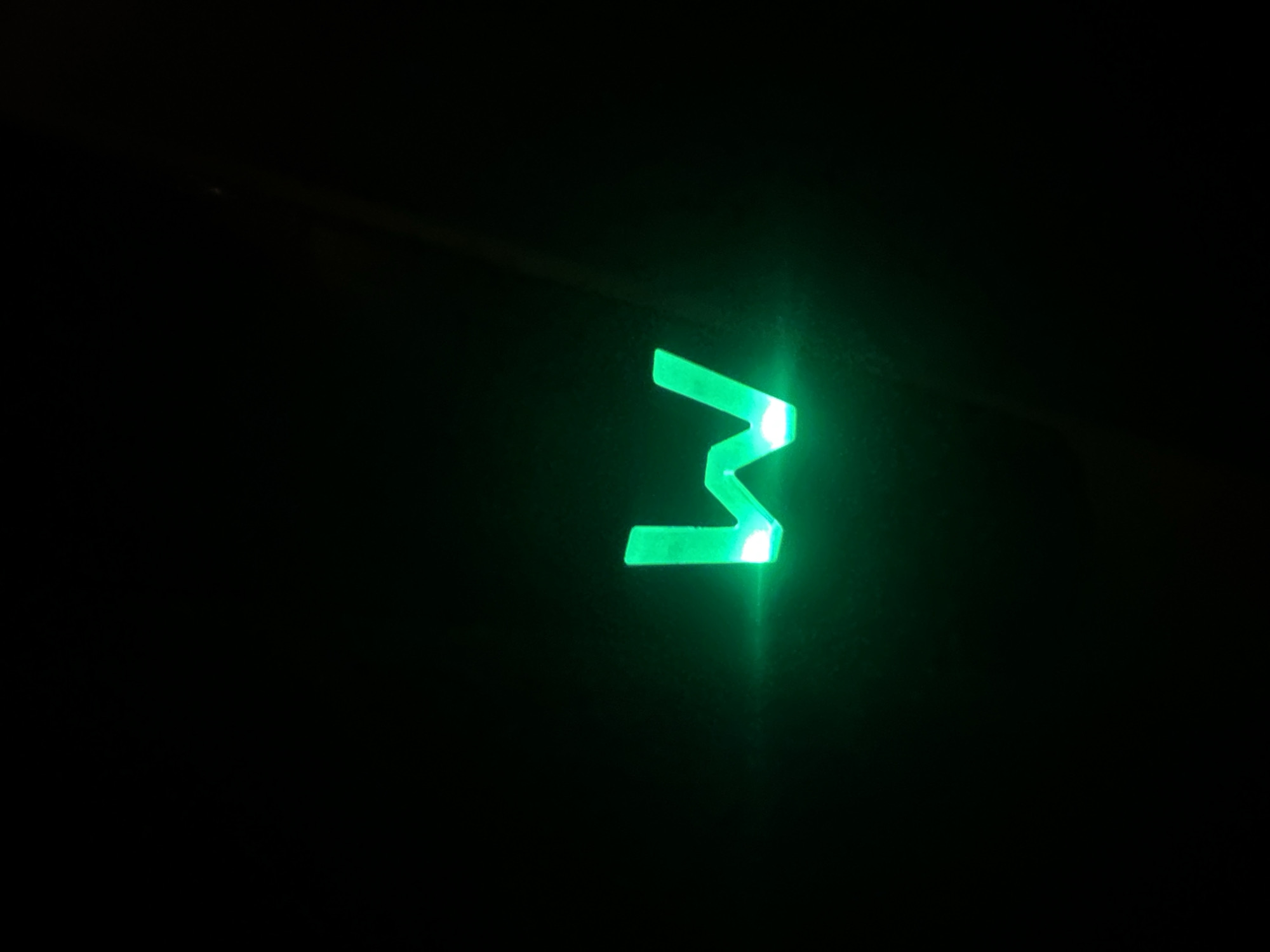 A neon green letter "w" glows against a black background. The letter is illuminated from within, casting a soft glow around its edges. The "w" appears to be a three-dimensional object, perhaps a sign or a sculpture. The background is uniformly dark, with no discernible features or context. There are no people, animals, or other objects visible in the image. The lighting is dim, except for the bright glow of the letter "w." The overall impression is one of simplicity and focus on the illuminated letter. There is no information available to determine its location in Minsk, Belarus.