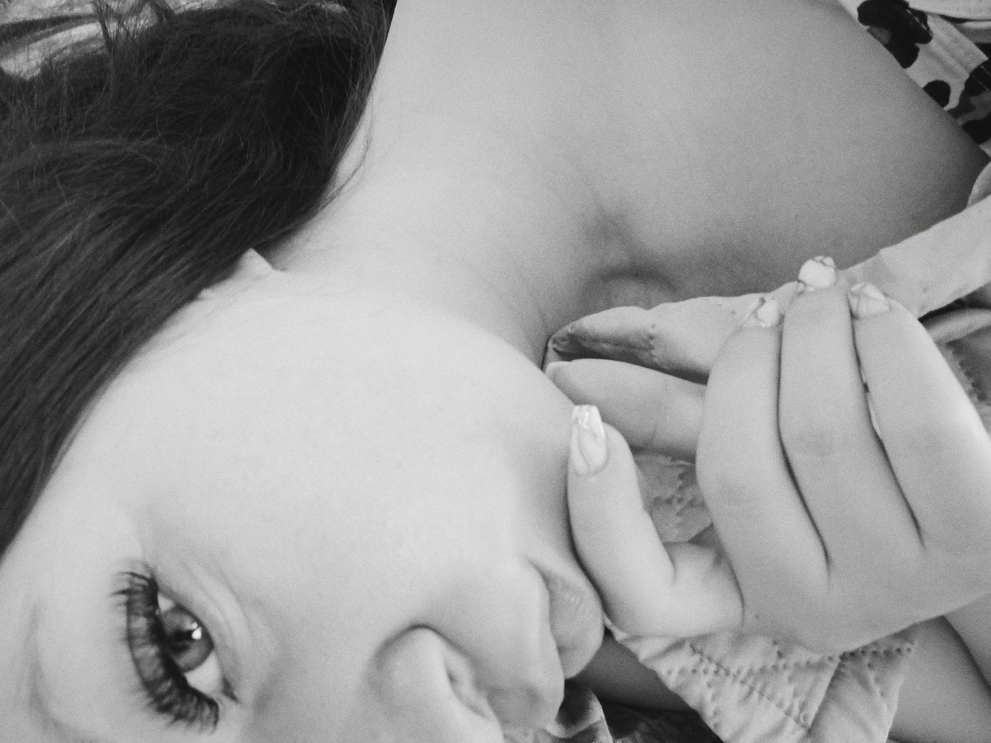 A close-up black and white photograph depicts a woman lying on her side, angled towards the camera. Her left eye, enhanced with prominent eyelashes, is visible. Her left hand is raised near her face, with fingers touching her cheek. Her bare shoulder and neck are exposed. Hair is visible on the left side of the frame. Part of a patterned garment is near the top right. No location in Tobolsk, Russia is determinable from the image.