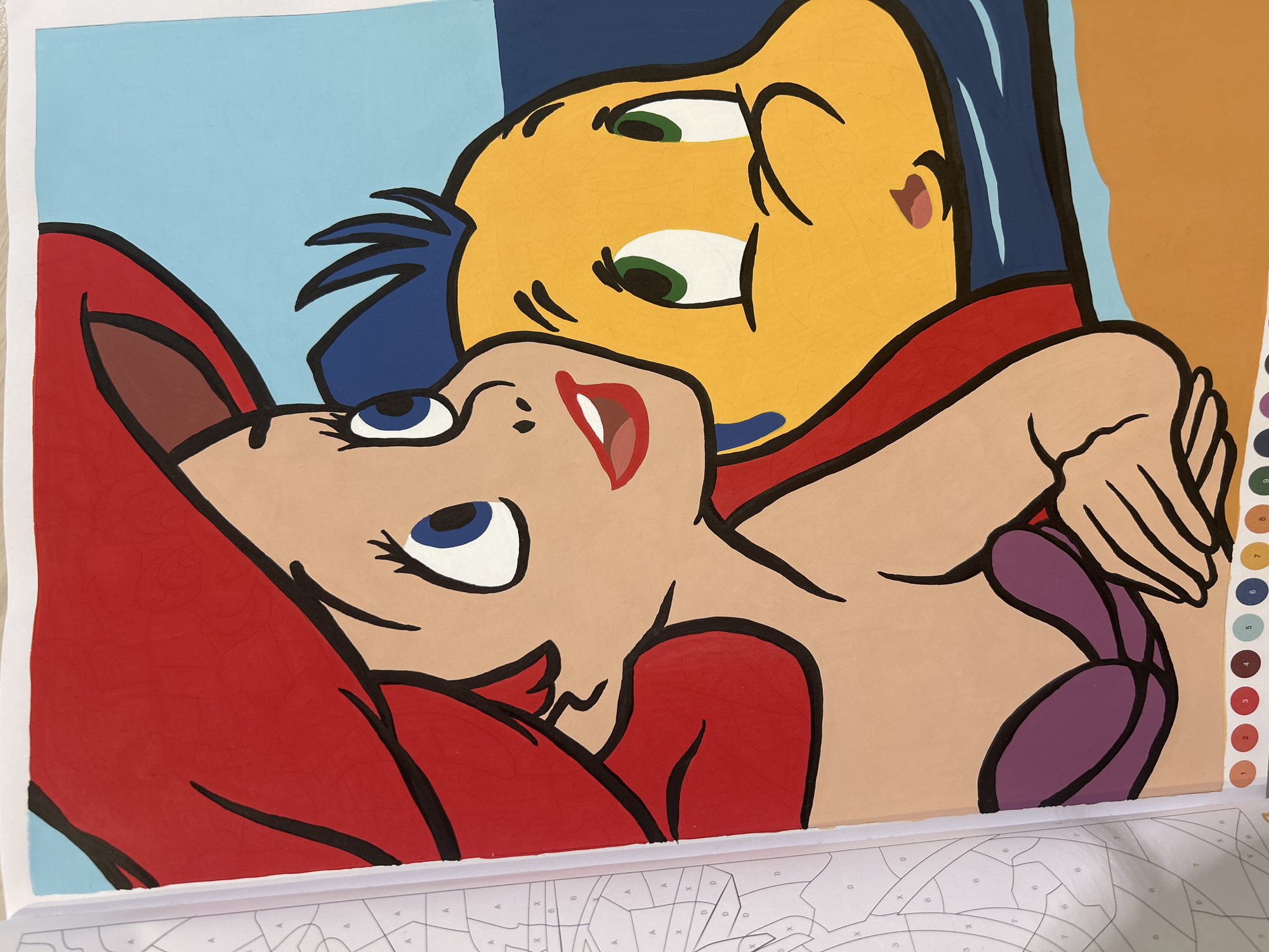 The image shows a partially completed paint-by-numbers artwork featuring the characters Ariel and Flounder from Disney's "The Little Mermaid." Ariel, a young woman with red hair, is depicted from the chest up, looking to her right with wide blue eyes. Her red hair is prominent, framing her face, and she is wearing a purple seashell-shaped bikini top. Beside her, to her right, is Flounder, a yellow fish with green eyes, also looking to his right with a surprised expression. The background consists of light blue and darker blue sections, suggesting water and sky. The artwork is laid out on a table next to an open paint-by-numbers book. The book's pages show numbered outlines of various shapes and areas, corresponding to the colors used in the painting. A row of numbered paint pots, labeled 1 through 9, is visible at the bottom of the painting. The paint has been applied to the canvas in solid blocks of color, with black outlines defining the shapes of the characters and their features. The surface of the paint shows some subtle cracking, indicating it may be drying or has dried.