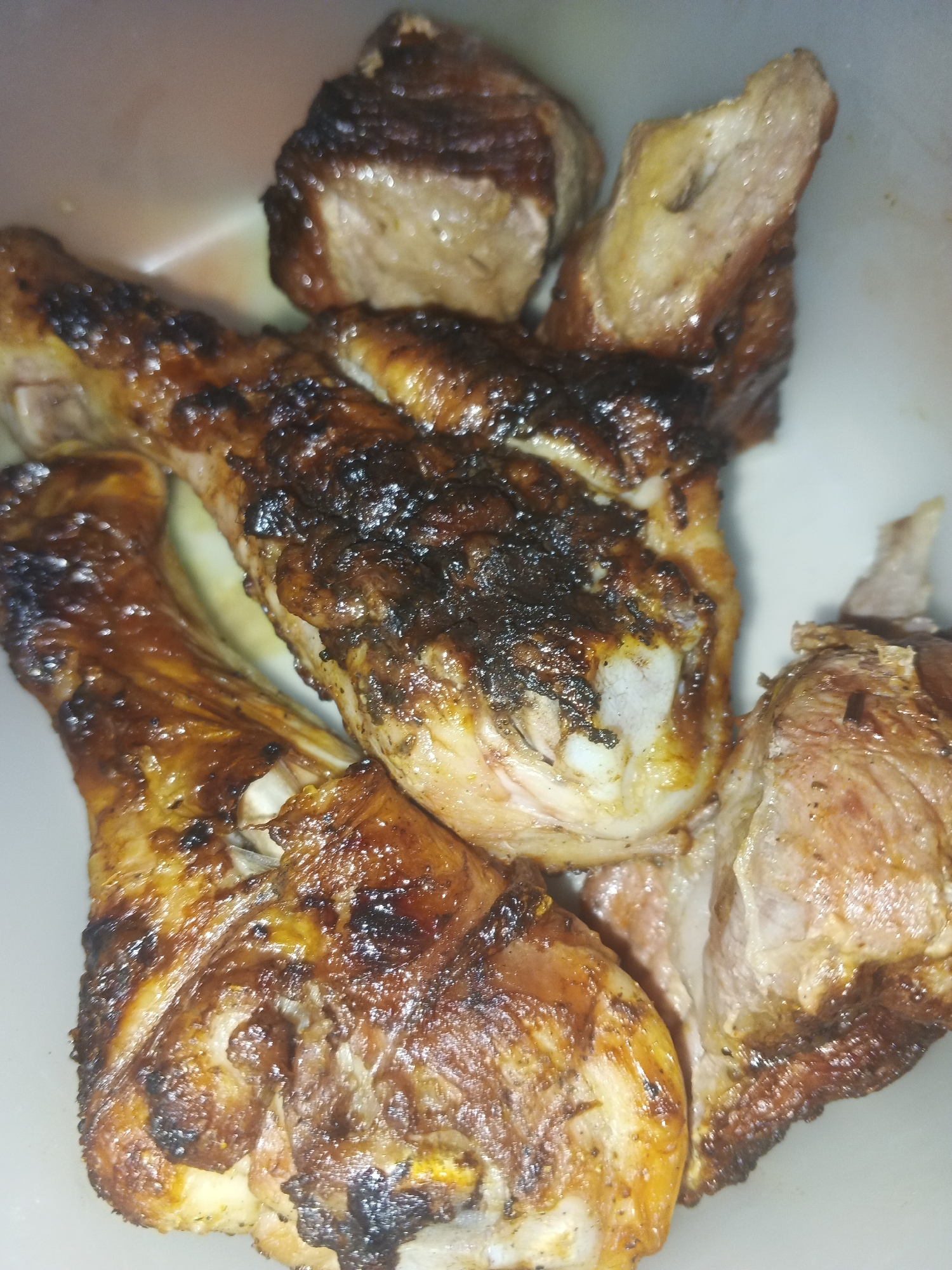 The image shows a close-up of cooked meat, likely chicken drumsticks and chunks of other meat. The meat appears to be grilled or roasted, with some charring. The food is placed in a white bowl or container. There is no information to suggest the image was taken in Rusalevka, Russia. There are no people or actions visible in the image.