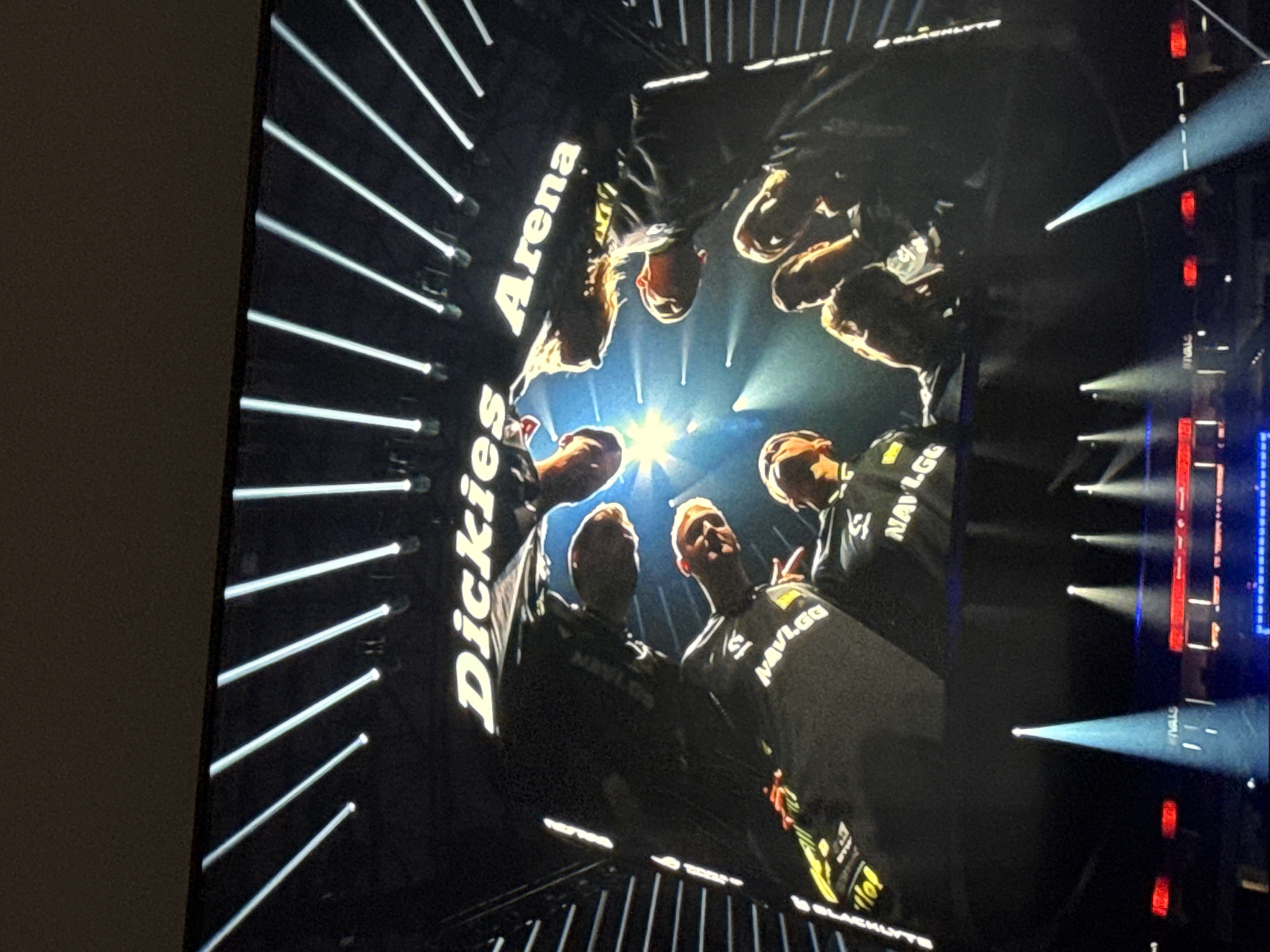 The image shows a low-angle shot of a huddle of individuals wearing NAVI.GG branded apparel, potentially a sports team or esports team. The location appears to be the "Dickies Arena", indicated by signage in the image. The lighting is dramatic, with bright spotlights shining upward and creating silhouettes of the people. There are vertical lines and lights suggesting an indoor arena or stadium. The overall setting indicates a competition or performance event, possibly within the city of Sofia, Bulgaria.