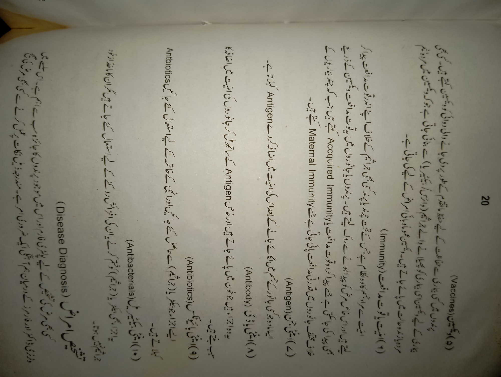 This image is a scanned page from a book, likely a biology or medical textbook, written in Urdu. The content discusses medical terms and concepts such as vaccines, immunity, antibodies, antigens, and antibiotics. The page is numbered '20' in the top right corner. The text is arranged in columns with numbered points and English transliterations in parentheses. There are no people, objects, or environmental elements depicted beyond the scanned page itself. There is no information within the image to suggest a location in Mansehra, Pakistan.