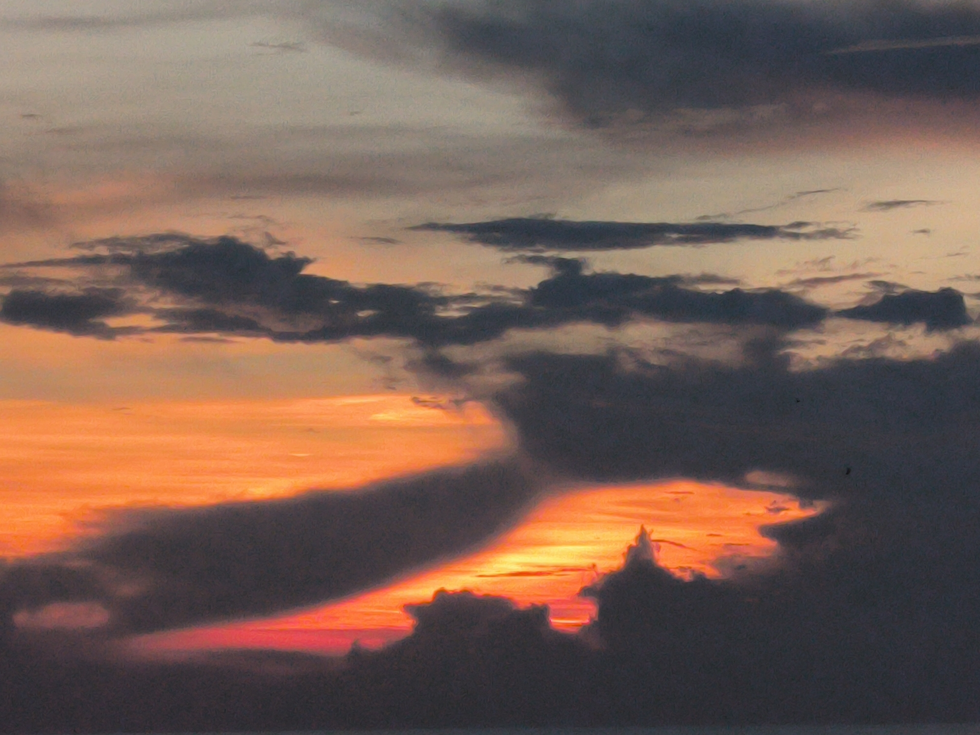 The image captures a sunset scene, likely in Lhokseumawe, Indonesia, given the prompt. The sky transitions from a greyish-white at the top to a vibrant orange and red near the horizon. Dark, heavy clouds dominate the view, partially obscuring the sunset. The clouds are arranged in layers, with some appearing as thin streaks and others as large, dense formations. The light from the setting sun illuminates the edges of the clouds, creating a stark contrast between the bright colors of the sky and the dark shapes of the clouds. The bottom of the image suggests a body of water, possibly the sea, with a faint, dark line representing the horizon.