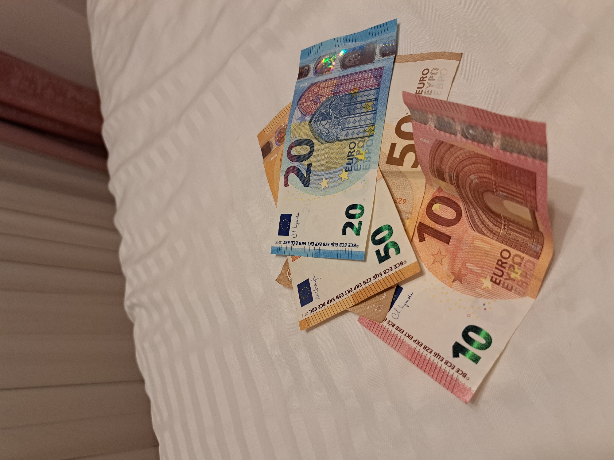 A close-up shot presents a collection of euro banknotes scattered on a white, striped surface. The bills include a 20 euro note, a 50 euro note, and a 10 euro note. These banknotes are slightly crumpled. The background is a plain white fabric with faint, parallel stripes. The location in the city of Negovan, Bulgaria is not discernible from the image.