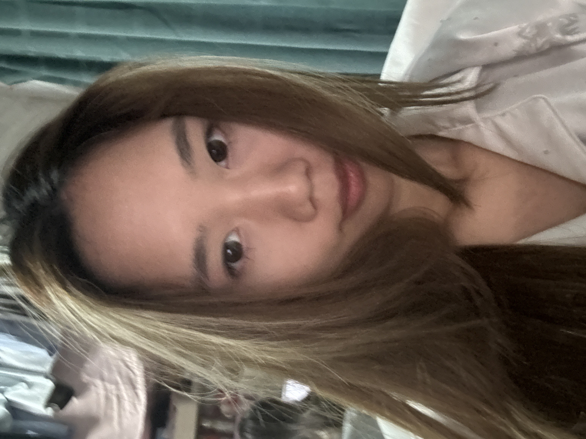 A close-up, rotated headshot photograph shows a young woman with brown hair and light brown highlights. The background features a blurry, light blue fabric. The woman is wearing a light-colored collared shirt or pajamas. The image does not provide information to determine location in the city of Nan'an District, China.