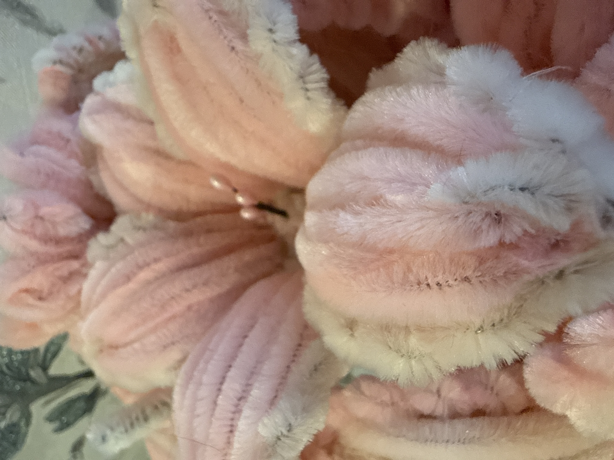 The image shows a close-up of pink and white plush flowers. The petals are textured with ribbed or striated patterns. There is a hint of gray-patterned material in the background. The image appears to be taken indoors, with soft, diffused lighting. The location Марковский, Russia is irrelevant as the image does not contain any indicators relating to it.