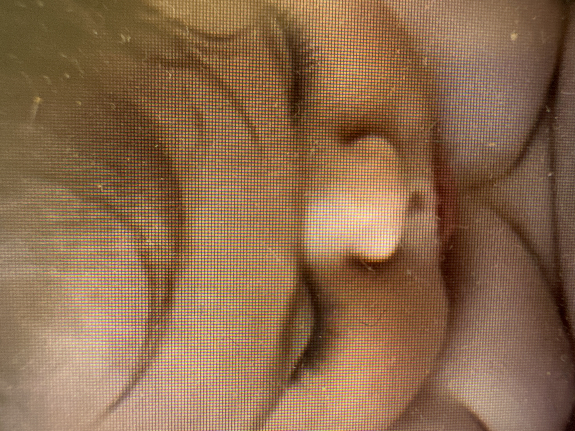 The image is a close-up, pixelated photograph of a baby's face, taken from a low angle. The baby's eyes are closed, and its face is partially obscured by shadows. The skin tone is fair, with rosy cheeks. The lighting is warm and somewhat diffused. The background is out of focus and appears to be dark. The image quality is low, with visible pixelation. No specific location in Murcia, Spain, can be identified from this image.
