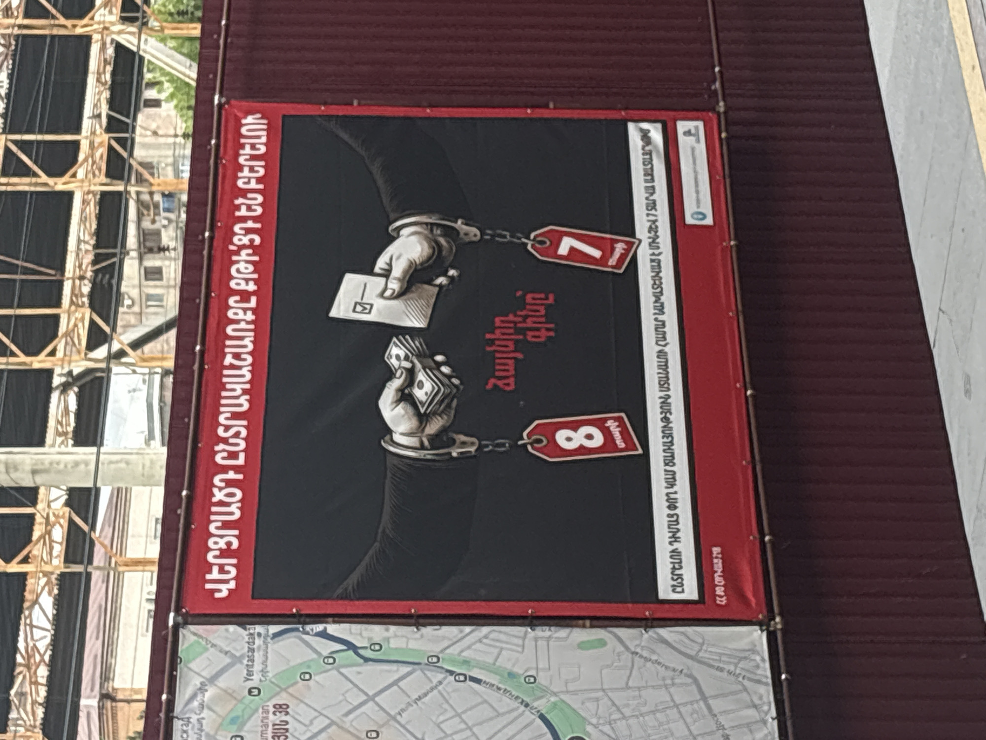 The image shows a vertical advertisement on a maroon-colored wall. The ad features two hands in handcuffs, one holding a voting ballot and the other holding money. Price tags labeled "7 years" and "8 years" are chained to the handcuffs. Armenian text surrounds the image. Below the advertisement, a map shows the location near Yeritasardakan and Umanian street, Yerevan, Armenia. A structure of girders and beams is visible behind the advertisement.