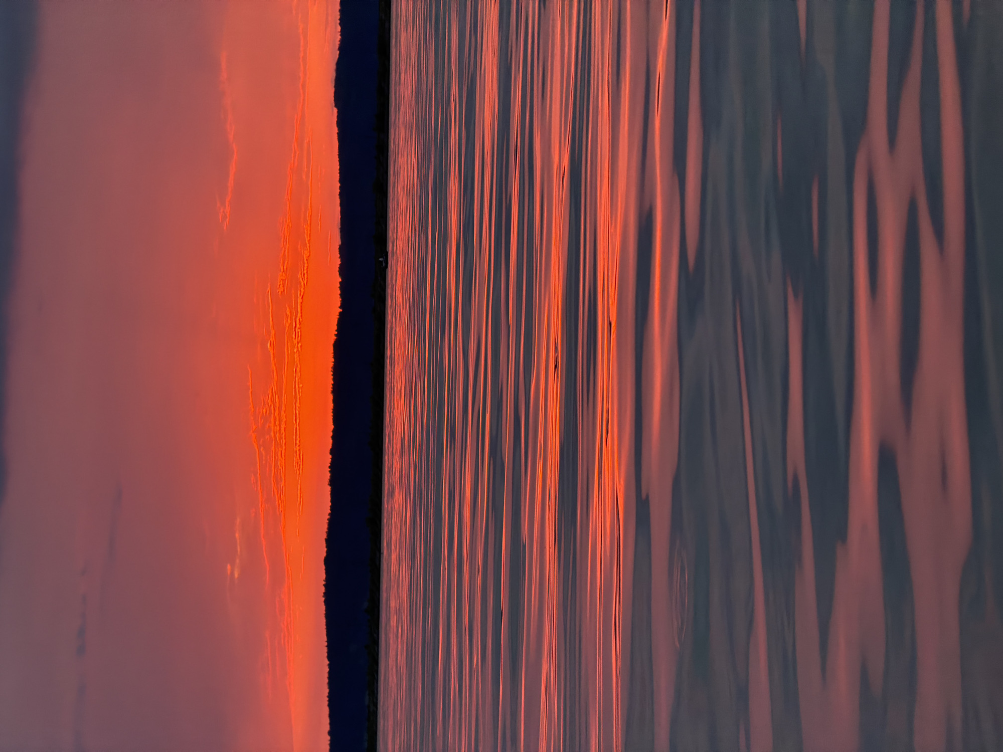 A body of water reflects a vibrant sunset. The sky transitions from a deep purple at the top to a fiery orange and red near the horizon, with scattered clouds. The water's surface is rippled, creating a pattern of light and shadow that mimics the colors of the sky. A dark, silhouetted tree line forms the horizon. In the distance, a small boat with a person is visible on the water. The scene appears to be on the Kama River in Chaikovsky, Russia.