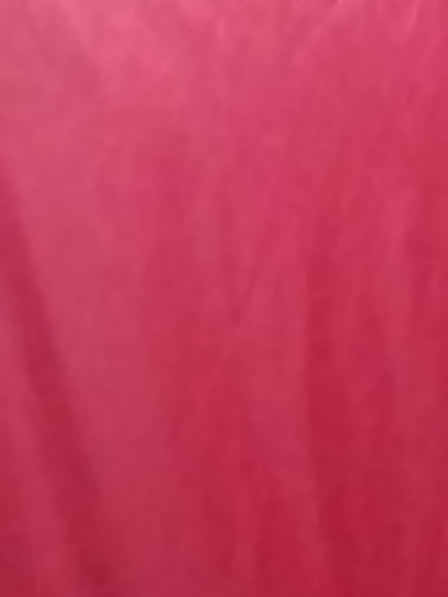 The image is a close-up, full-frame shot of a textured, solid pink fabric. There are subtle variations in lighting and shadow across the surface, suggesting folds or a slightly uneven texture. No other objects, people, or environmental details are visible. The location is not discernible from the image.