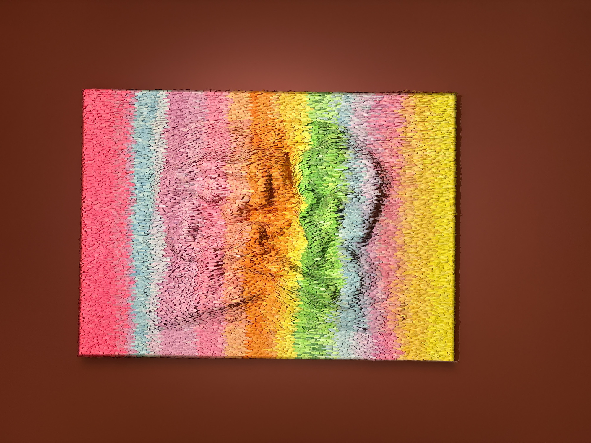 A photograph depicts a rectangular artwork featuring a relief of a person's face rendered in textured, colorful strokes, set against a solid brown background. The artwork consists of vertical stripes of pink, blue, purple, orange, yellow, green, and gray. The face is formed by the varying heights of the strokes within these color bands. The artwork casts a slight shadow on the background, suggesting it is mounted on a wall. There is no indication of the location in the city of Liangjiang, China.