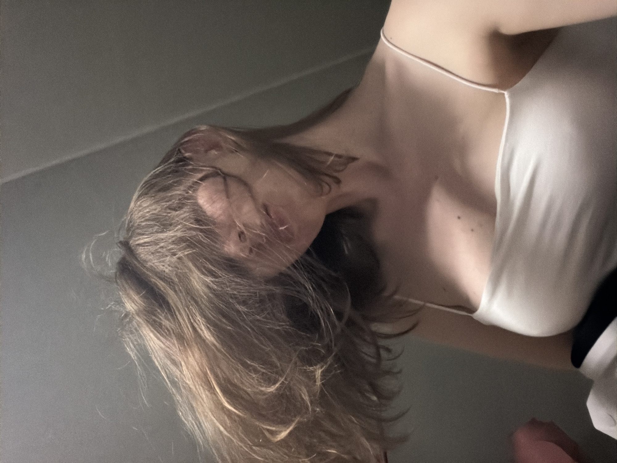 The media file shows a close-up, low-angle shot of a person's upper body, with their head tilted back and hair falling forward. The person is wearing a thin-strapped white garment. The background is a plain, light gray wall. The lighting is dim, suggesting an indoor setting at night or in a poorly lit room. The overall mood is intimate and somewhat melancholic, with the low angle and the subject's obscured face contributing to this feeling. No text is visible in the image. The location context provided is Dongducheon-si, South Korea.
