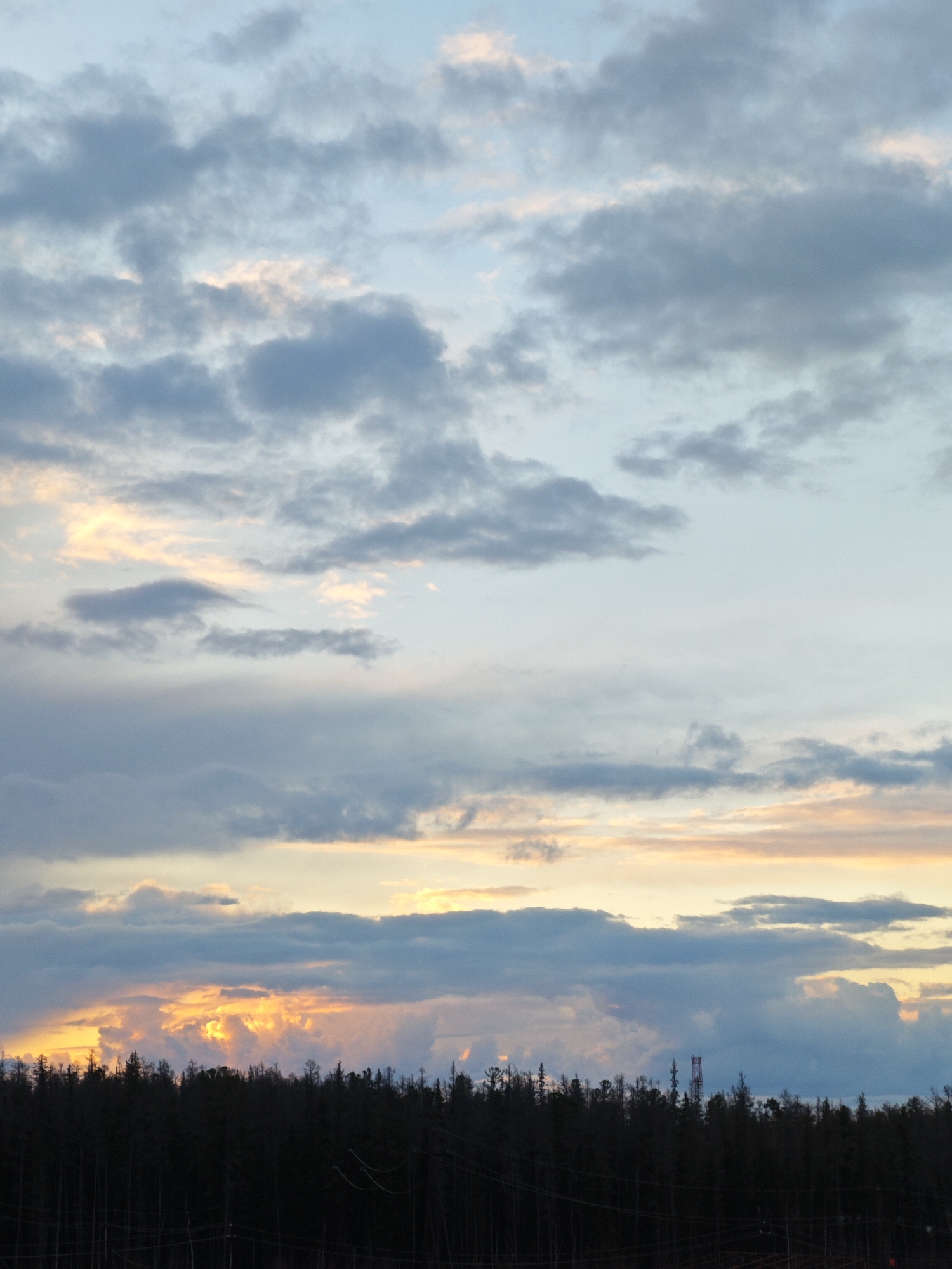 The image shows a sky with a mix of blue, gray, and orange clouds at sunset over a dark forest silhouette. A cell tower rises slightly above the treeline. The location is Unknown, Russia.