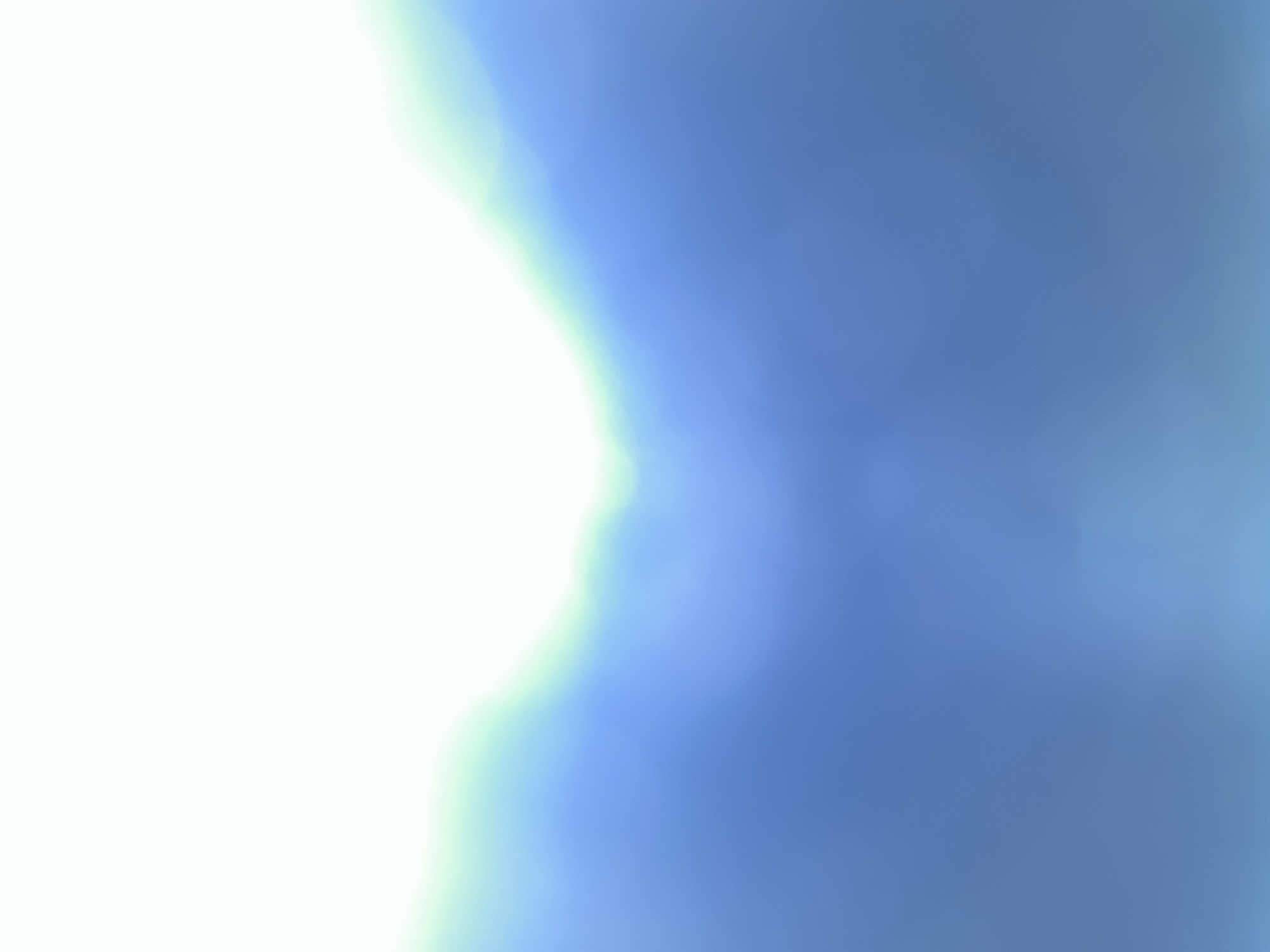 The image is an abstract, out-of-focus depiction of a bright white area transitioning into shades of blue, with a subtle hint of green at the transition point. The bokeh effect is prominent, creating soft, blurred circles of light. The composition suggests a gradient, with the brightest area at the top and darker blues towards the bottom. There are no discernible objects, people, or any identifiable location. The scene does not appear to be in Belgrade, Serbia, or any specific city.