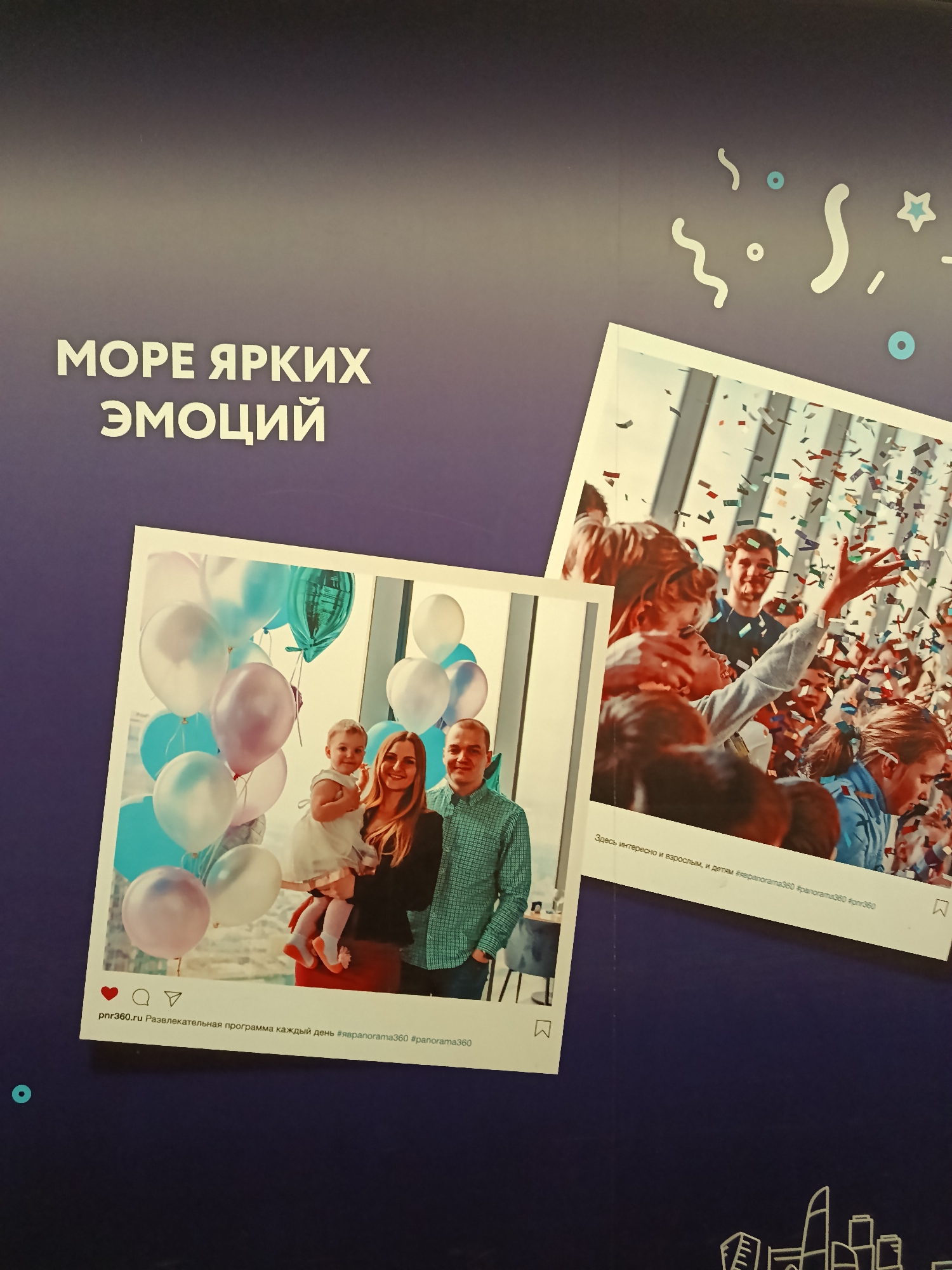 Here is a description of the image:
The image is a close-up shot of a promotional poster for a venue called "Panorama 360". The poster features a dark blue background that transitions to a lighter shade at the top, with white text that says "МОРЕ ЯРКИХ ЭМОЦИЙ" (Sea of Bright Emotions). Scattered around the text are whimsical white shapes resembling confetti or streamers.
Two Instagram-style images are displayed on the poster. The first shows a family—a man, a woman, and a young child—posing with a bunch of balloons against the backdrop of a large window. The text below this image reads "pnr360.ru Развлекательная программа каждый день #яврапогата360 #panorama360" (pnr360.ru Entertainment program every day #yavrapogata360 #panorama360).
The second image captures a celebratory scene with people under a shower of confetti. The text below this picture says, "Здесь интересно и взрослым, и детям #яврапогата360 #ралогата360 #pnr360" (Here it is interesting for adults and children #yavrapogata360 #ralogata360 #pnr360).
The bottom of the poster includes a sketched cityscape. The mention of Panorama 360 and the skyscrapers in the illustration suggest that this venue is likely located in Moscow, Russia, as Panorama 360 is a prominent observation deck in the Moscow City business district.