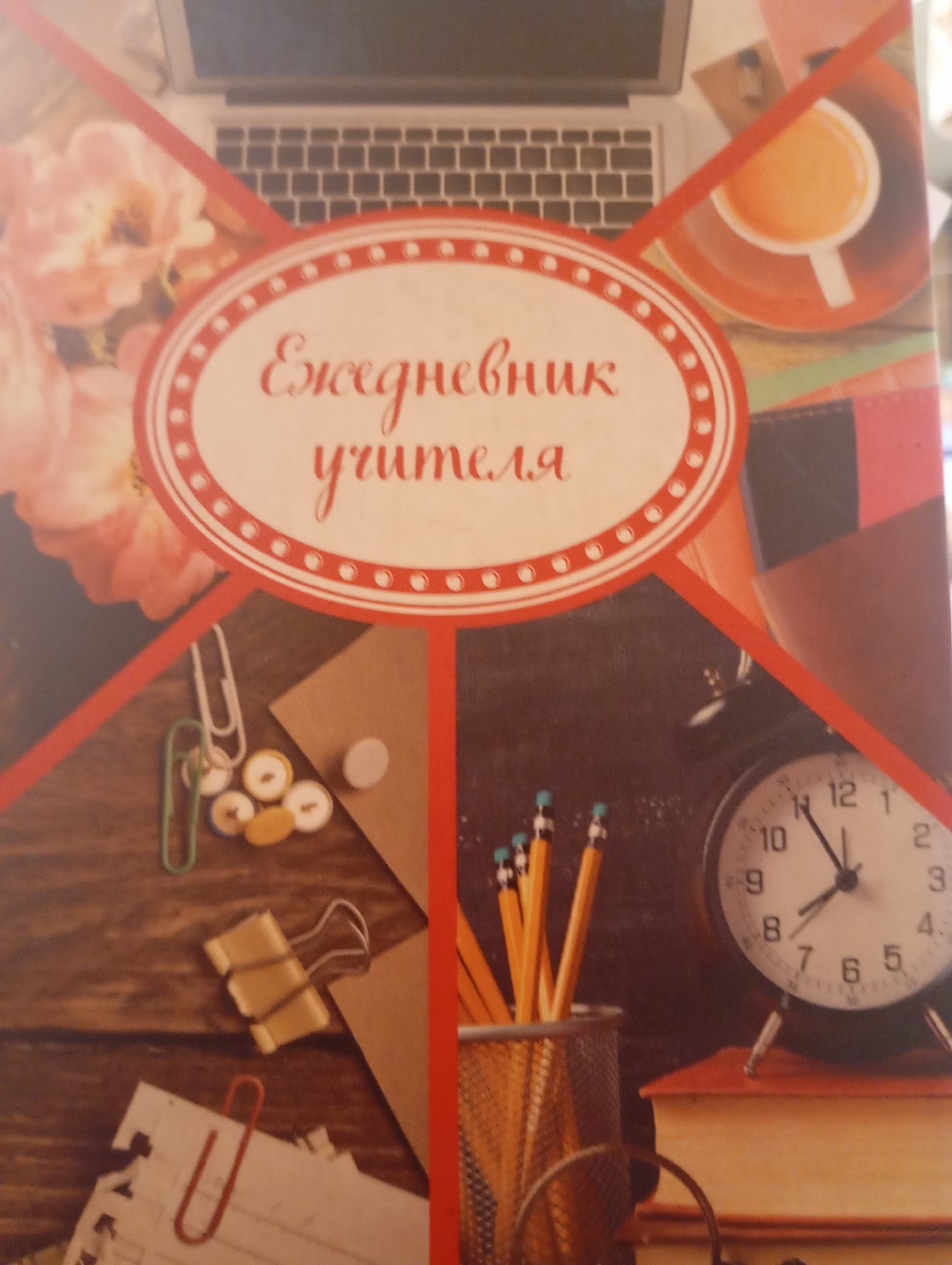 The image shows the cover of a planner, likely a school supply item, with the text "Ежедневник учителя" (Teacher's Diary) prominently displayed in a decorative oval frame. The background imagery is a collage of school-related items and decorative elements. On the left side, there are pink flowers and a portion of a laptop keyboard. The center of the cover features the planner's title. To the right of the title, there is an image of a cup of coffee or tea. The bottom half of the cover displays more school supplies: on the left, there are paper clips, push pins, and binder clips scattered on a wooden surface, along with torn pieces of paper held together by a red paper clip. In the bottom right, a pencil holder filled with sharpened pencils sits next to an alarm clock placed on top of a stack of books. The overall aesthetic suggests a collection of items relevant to a teacher's desk or workspace, presented in a visually appealing manner for the cover of a planner.
There is no information within the image that indicates its location in the city of Omsk, Russia. The image depicts a generic collection of objects and is not a scene from a specific geographical location.