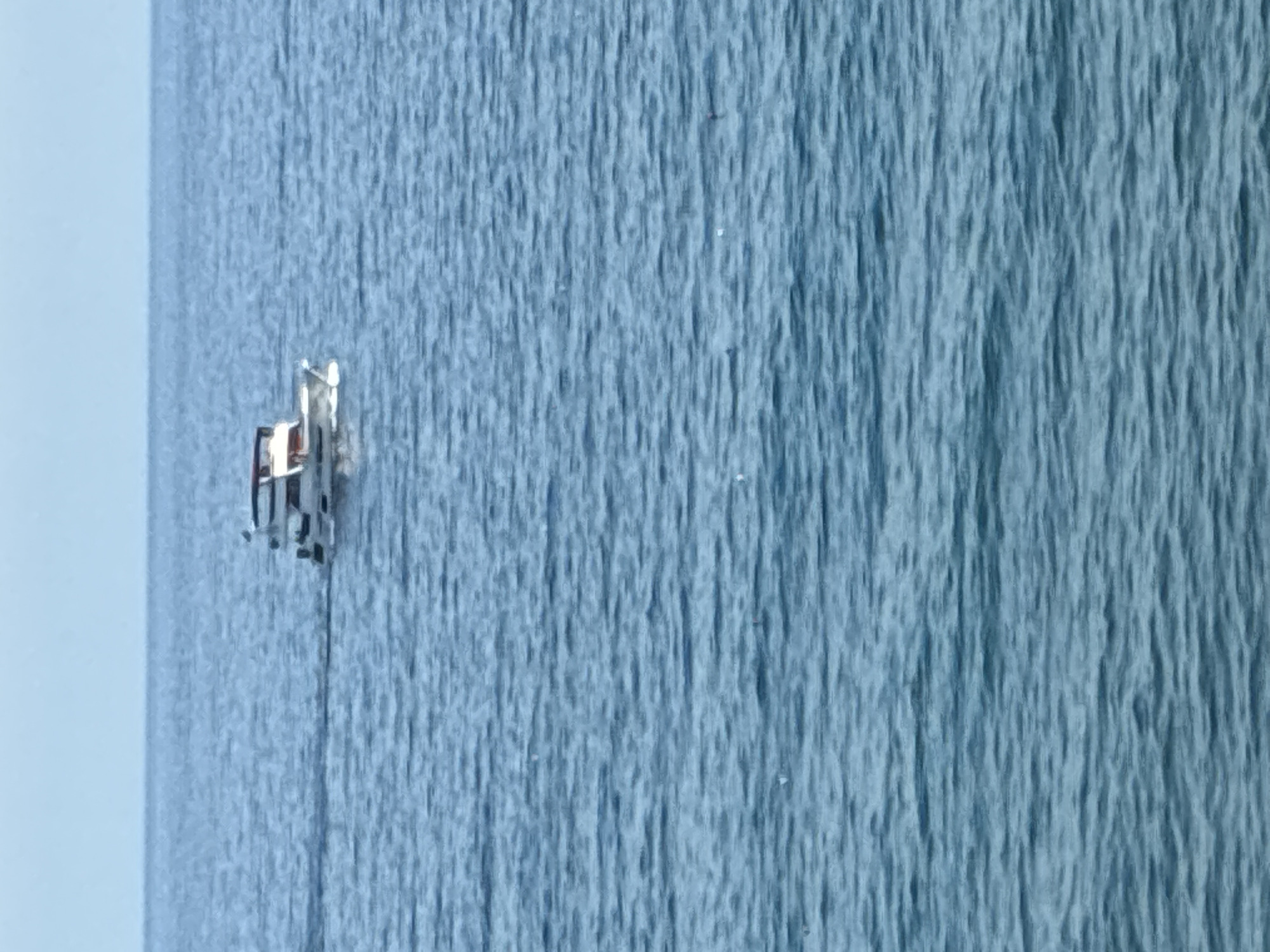 A small white motor yacht with a red canopy is moving across a calm blue sea under a pale sky. The yacht is positioned in the upper middle section of the image. The water is calm with gentle ripples. There are no other boats or landforms visible. The scene is set on the Mediterranean Sea, near Alanya, Turkey.
