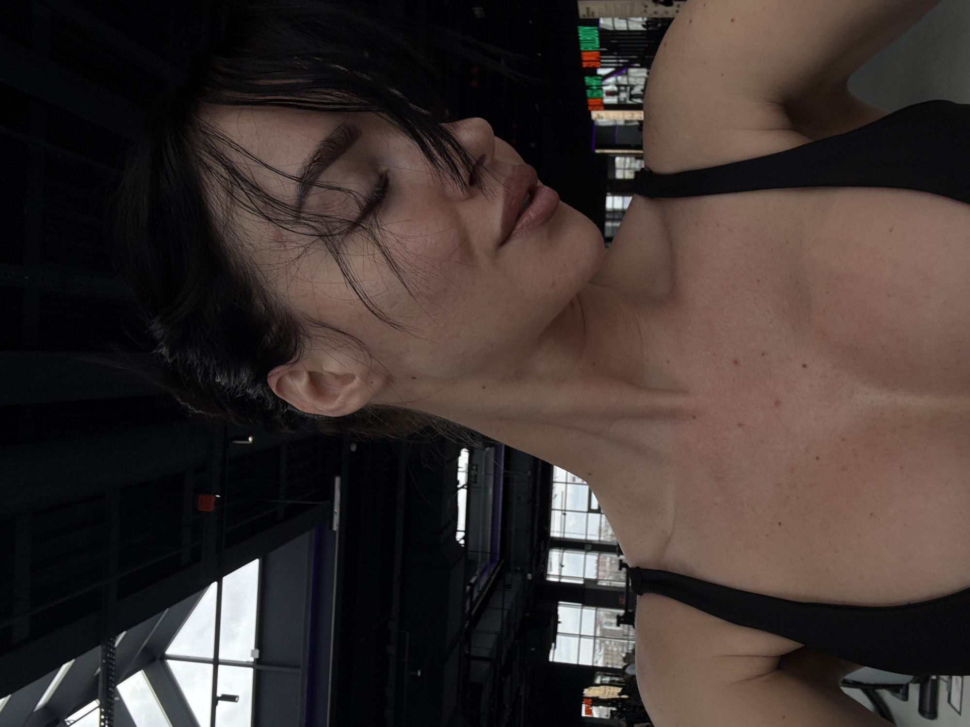 A woman with dark hair and closed eyes is seen in a close-up, angled shot. She is wearing a black top. The background features architectural elements, including windows and structural beams, suggesting an indoor location. The presence of the city of Krasnoyarsk, Russia cannot be confirmed from the image.