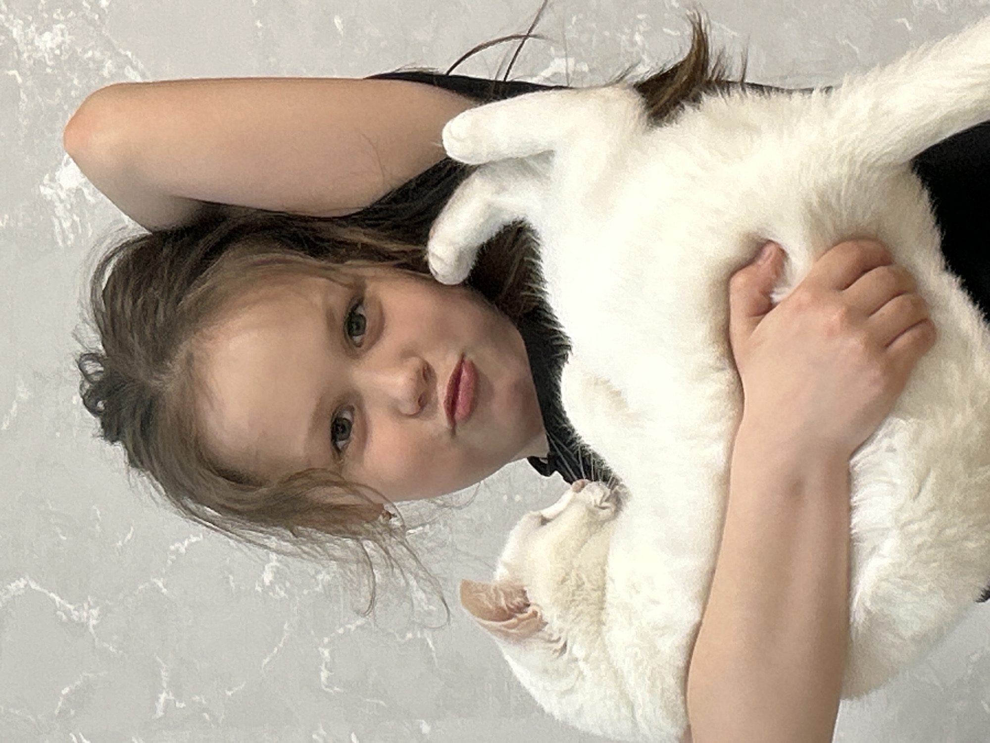 A young girl is holding a white cat. The girl has brown hair and is wearing a black shirt. The background appears to be a wall with a mottled pattern. The girl is lying on her side and holding the cat close to her. No specific location within Chaikovsky, Russia is identifiable.