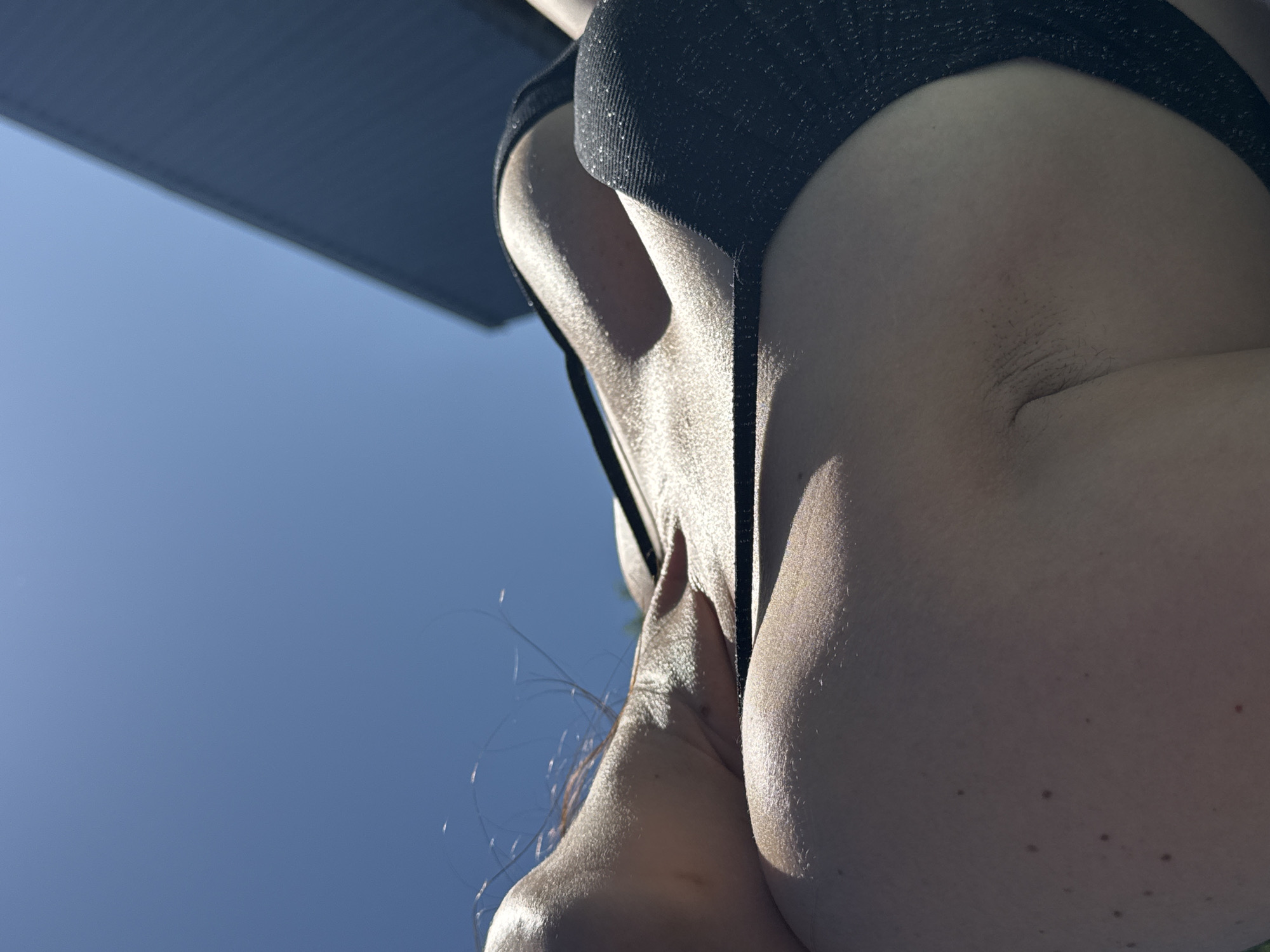 A low-angle shot captures a person wearing a black bikini bottom against a clear blue sky with a partial view of a building or structure in the top left corner. The person's skin is fair, and the view includes their armpit area and a portion of their torso. The angle emphasizes the upward perspective towards the sky. The location is not identifiable as Rusalevka, Russia from the provided image.
