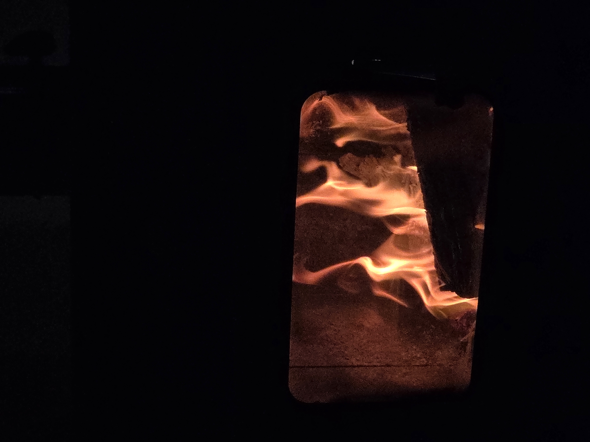 The image shows flames inside a wood-burning stove. The stove door appears to be made of heat-resistant glass, allowing a view of the fire within. The fire consists of orange and yellow flames, fueled by burning wood. The environment surrounding the stove is dark, indicating the image was taken in a dimly lit room. There is no discernible information regarding the location of Dulovo, Bulgaria.