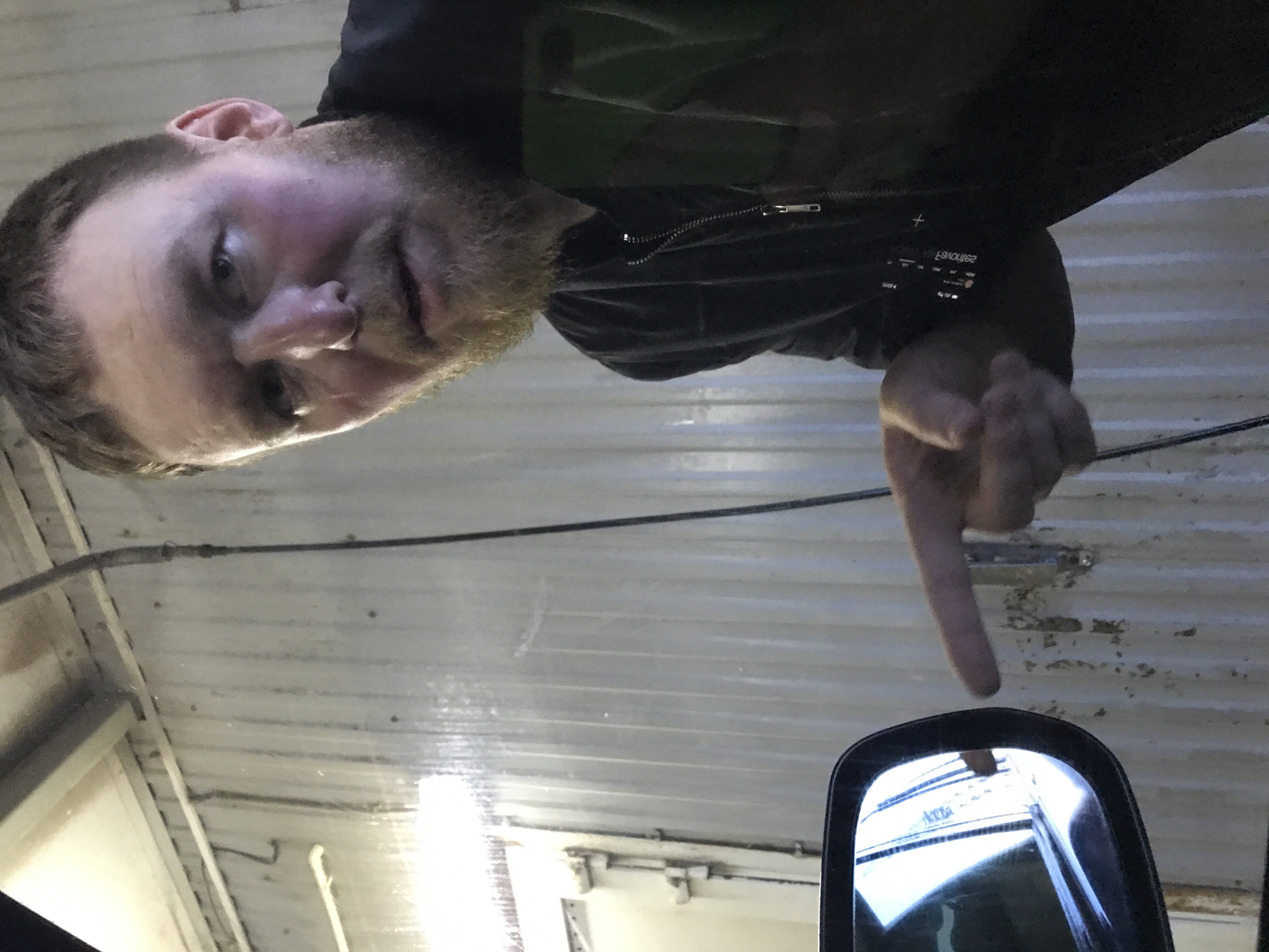 A man with a beard and short hair is pointing at a side mirror inside a vehicle. The interior roof of the vehicle is visible, appearing to be corrugated metal. No information is available about the exact location in the city of Chaikovsky, Russia, as the photo does not contain any identifiable landmarks or contextual cues to pinpoint a specific place.