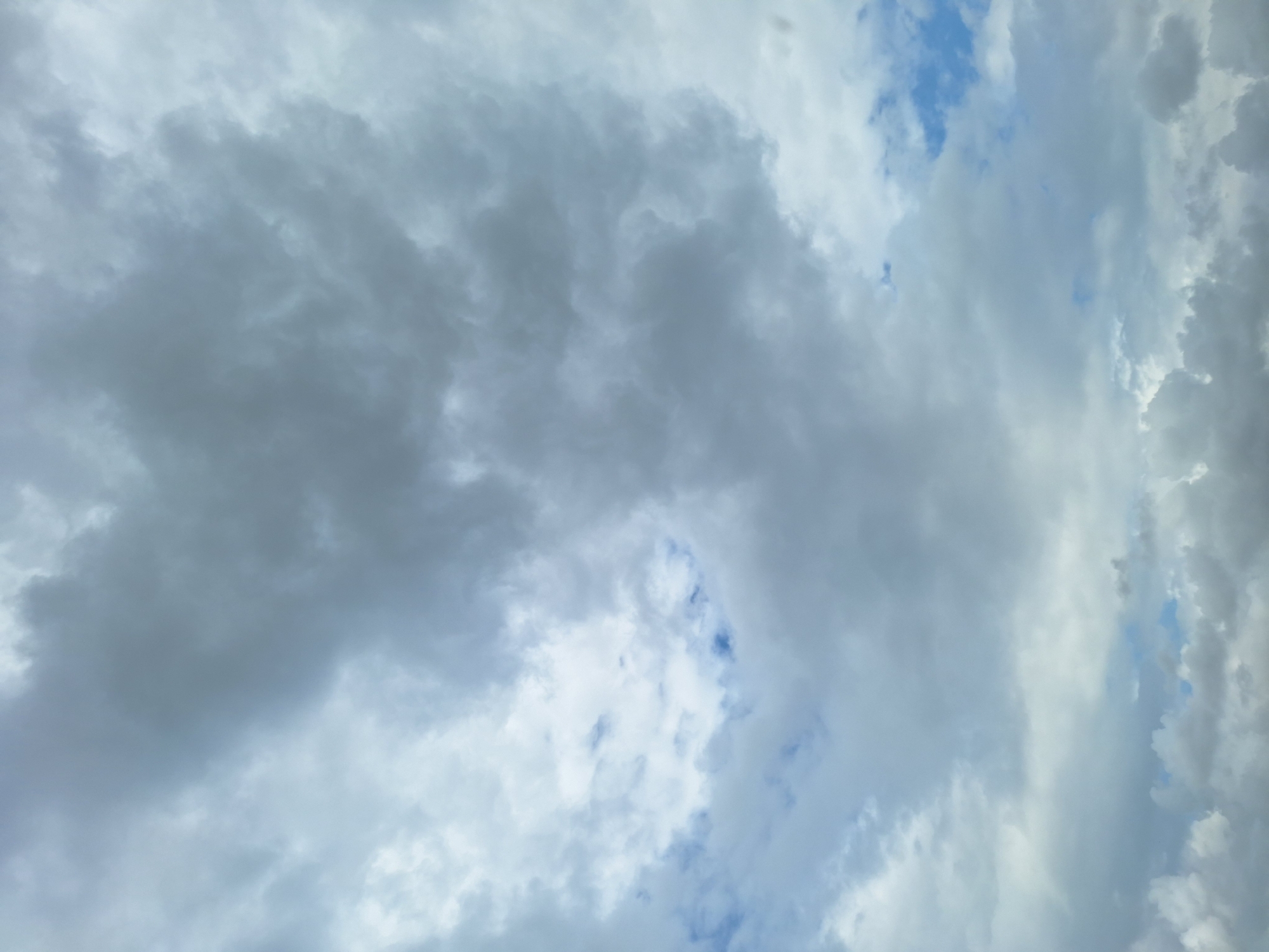 The image shows a cloudy sky with patches of blue visible in the distance. The clouds are varied in density and color, ranging from light gray to dark gray, with some areas appearing almost white. The lighting suggests it is daytime, but the heavy cloud cover indicates overcast or partly cloudy conditions. There are no people, structures, or discernible landmarks visible in the frame, making it impossible to determine a specific location within ჩიბათის თემი, Georgia, or any other city. The scene is purely atmospheric, focused on the natural phenomenon of cloud formations against a sky backdrop.