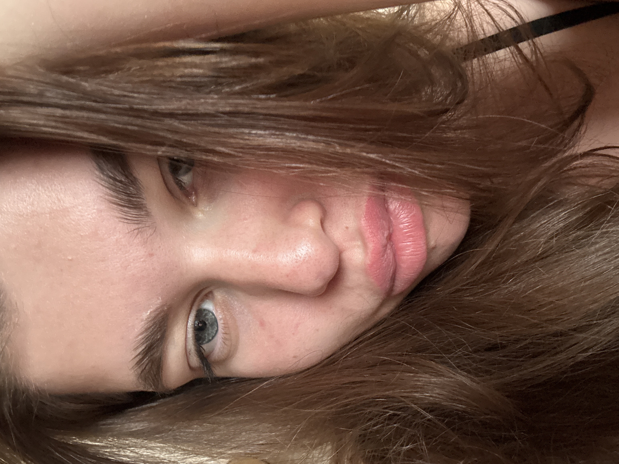 A close-up, slightly rotated image of a person's face, primarily capturing the left eye, nose, and lips. The person has fair skin, light-colored eyes, and light brown hair that frames their face. A dark strap or clothing detail is visible near the top right corner of the image. The background is out of focus, composed of the person's hair. There is no indication of the location being Мещёры, Russia, or any discernible environmental details.