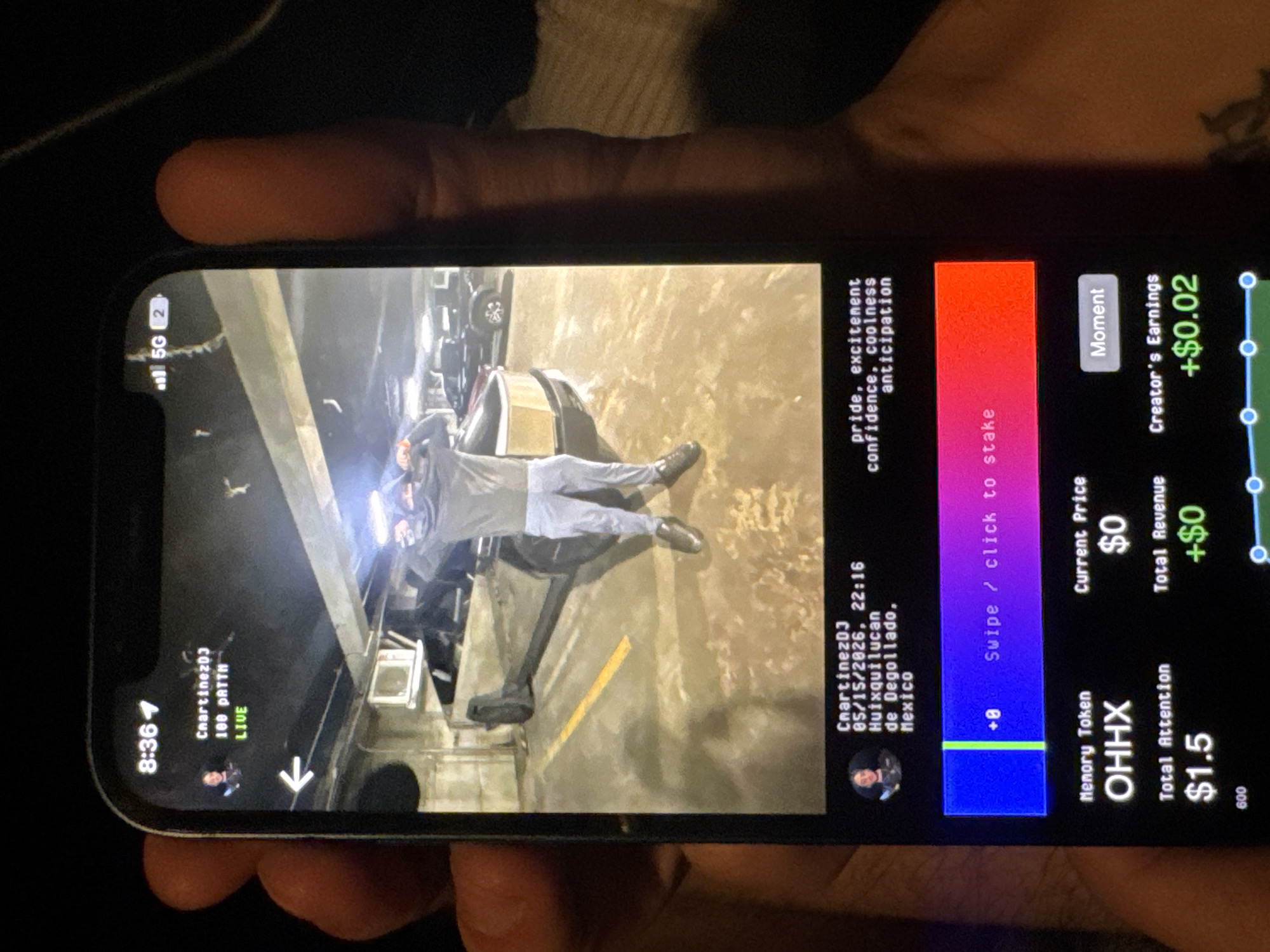 The image shows a person holding a phone displaying a live video. The video features a person in a light-colored outfit laying on a mechanism on a city street. The phone screen also shows on-screen elements like user profiles, timestamps ("8:36" and "05/15/2026, 22:16"), usernames ("ChartinezD3", "ChartinezDJ"), location ("Huixquilucan de Degollado, Mexico"), and a live indicator. Other details on the screen indicate revenue, prices, and token information. The time and date on the display are consistent with the time and date of the upload of the image.