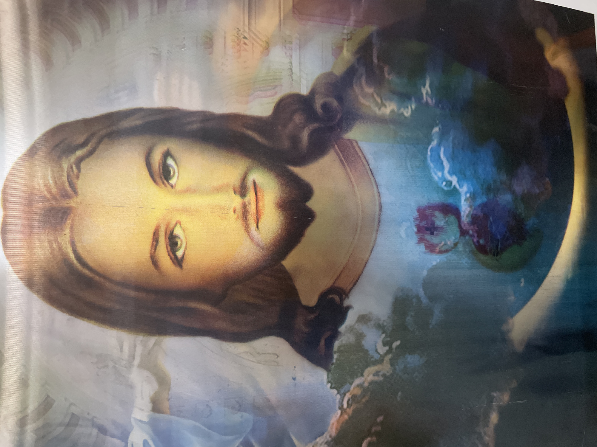 The image depicts a painting of Jesus Christ. He has long brown hair, a beard, and fair skin. He is wearing a white robe and is surrounded by a blue and white background. The location is unknown, but is likely NOT located in Izhevsk, Russia.