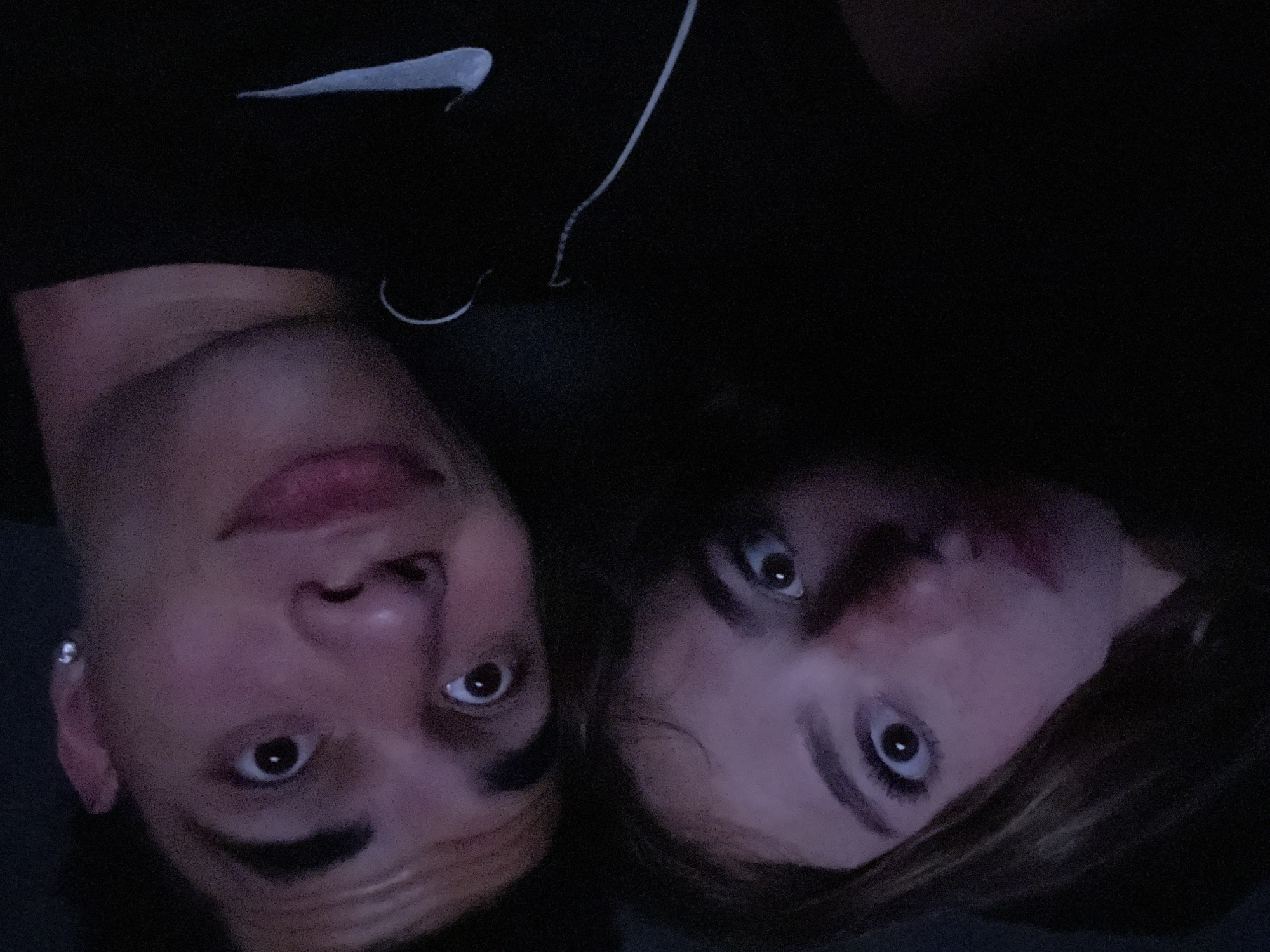 Two people are visible in the image, a male and a female, positioned side-by-side. The male is on the left, wearing an earring in his left ear. The female is on the right. Both are looking upwards at the camera. The male is wearing a black shirt with a white Nike logo on the upper left. The background is dark and indistinct. There are no identifiable landmarks or features that would associate the location with Heroica Puebla de Zaragoza, Mexico.
