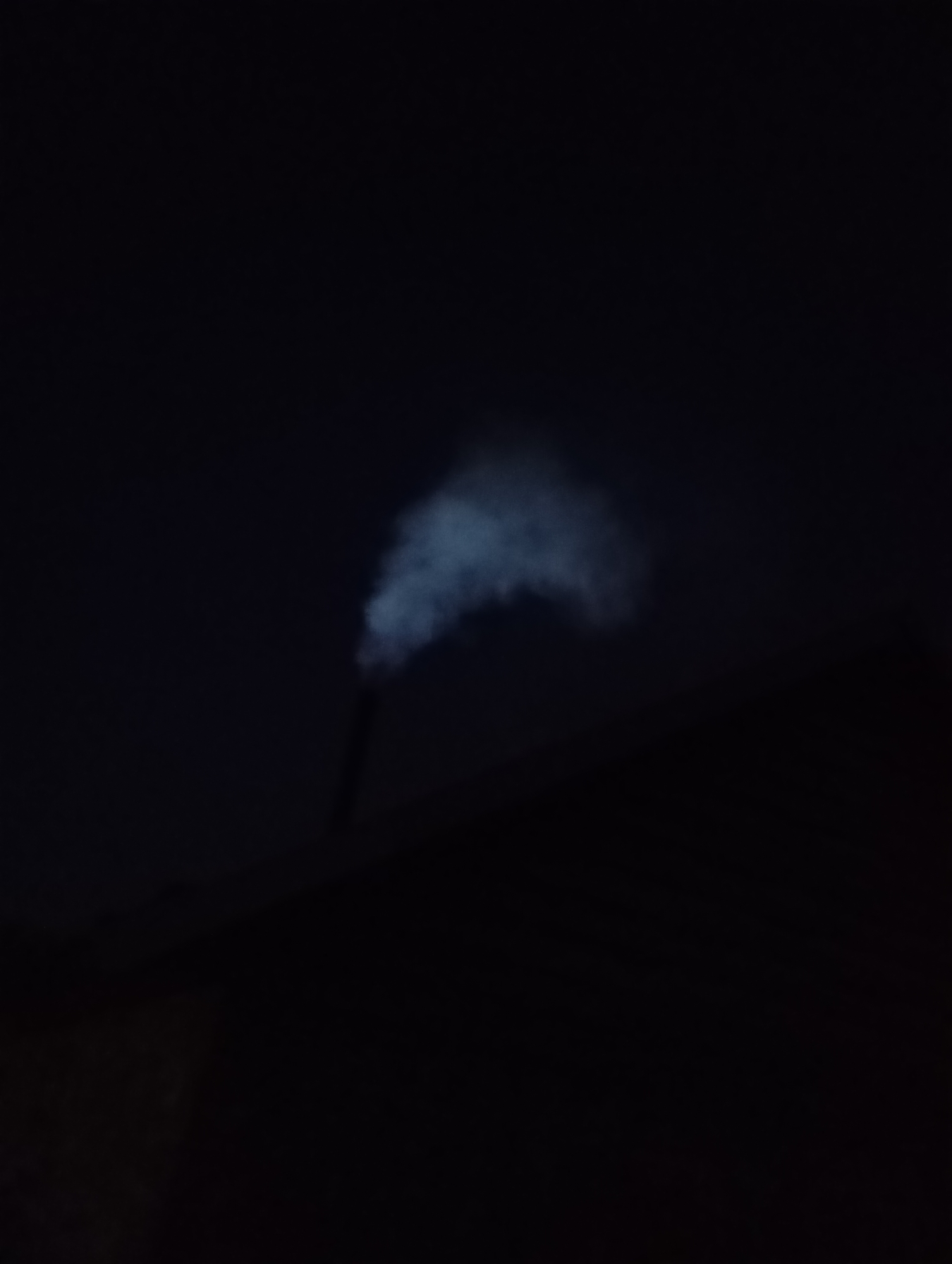 At night, smoke rises from a chimney atop a dark structure. The location is the city of Unknown, Unknown.