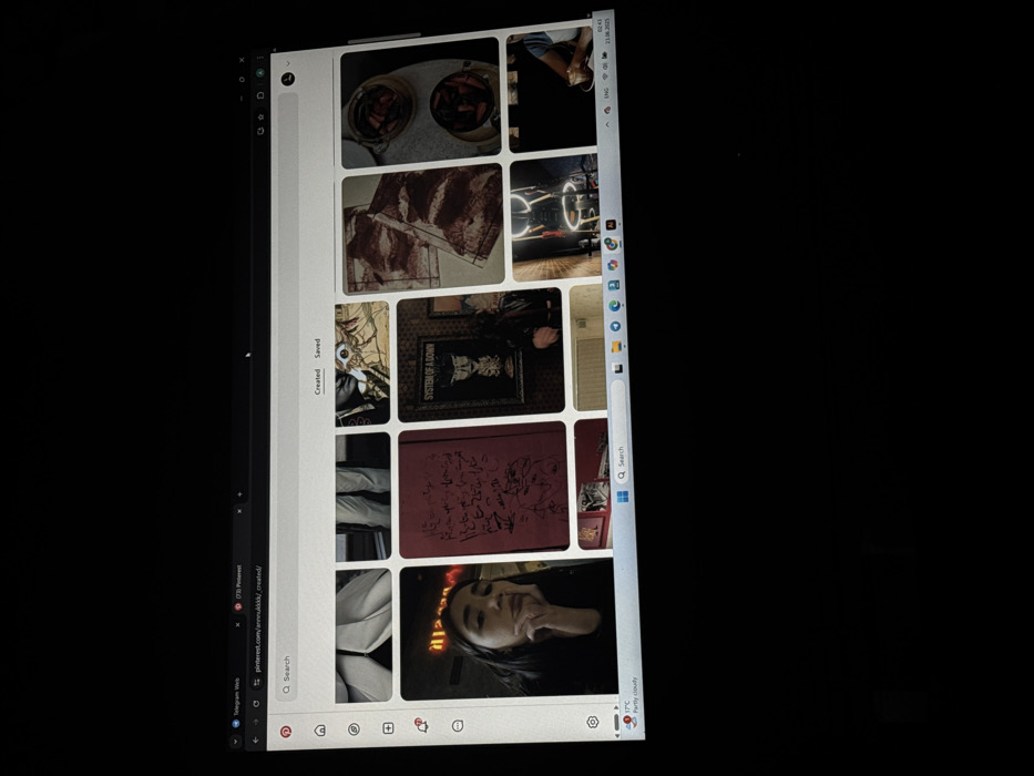 A vertical shot captures a computer screen displaying the Pinterest website. A collection of images fills the Pinterest board, including jars filled with food, artistic patterns in brown and white, a ring light setup, a framed System of a Down band poster, a red book with scribbled drawings, and a photo of a person's face with neon lighting. Below the Pinterest window, the Windows taskbar displays icons for Telegram Web and a search bar. The top right corner indicates the date and time.