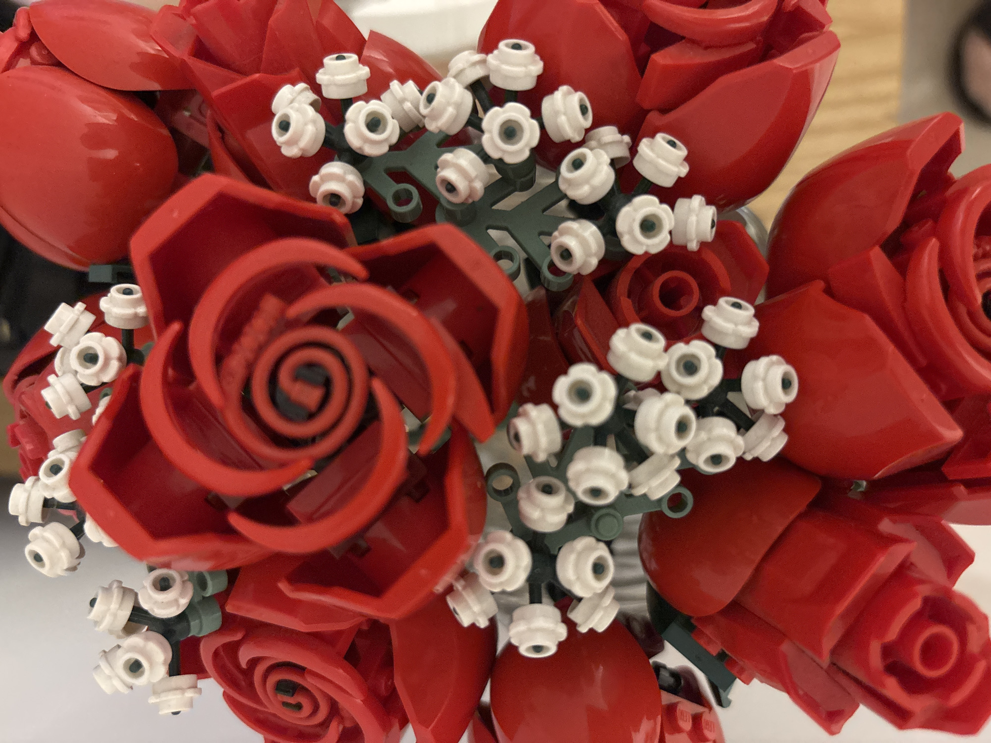 The image shows a bouquet of Lego flowers, primarily red roses with some white floral accents on green stems. The roses are constructed from red Lego pieces, forming the petal shapes. The white flowers appear to be assembled from smaller, round Lego components. The bouquet is densely packed, with multiple flowers overlapping. The setting is unclear and there is no indication of the location being Buenos Aires, Argentina.