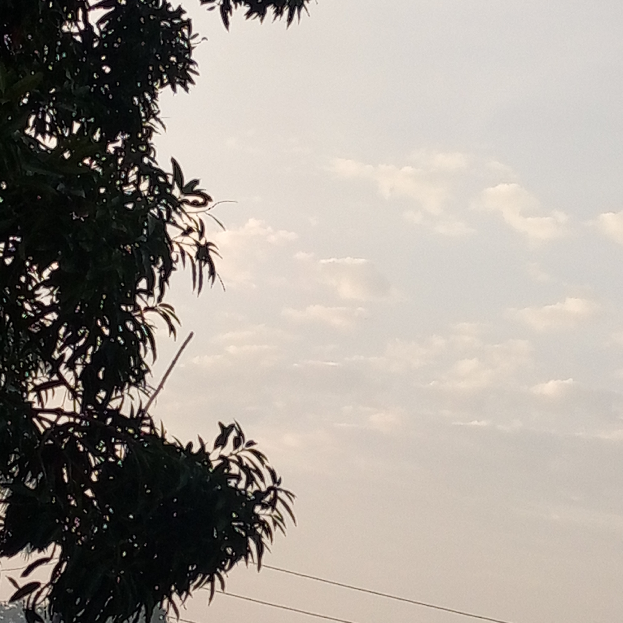 The image depicts a cloudy sky with tree foliage obscuring the left portion of the frame. Two power lines are visible running horizontally across the lower portion of the frame. The location is identified as Mararaba, Nigeria. No people, subjects, objects, actions or interactions are visible.
