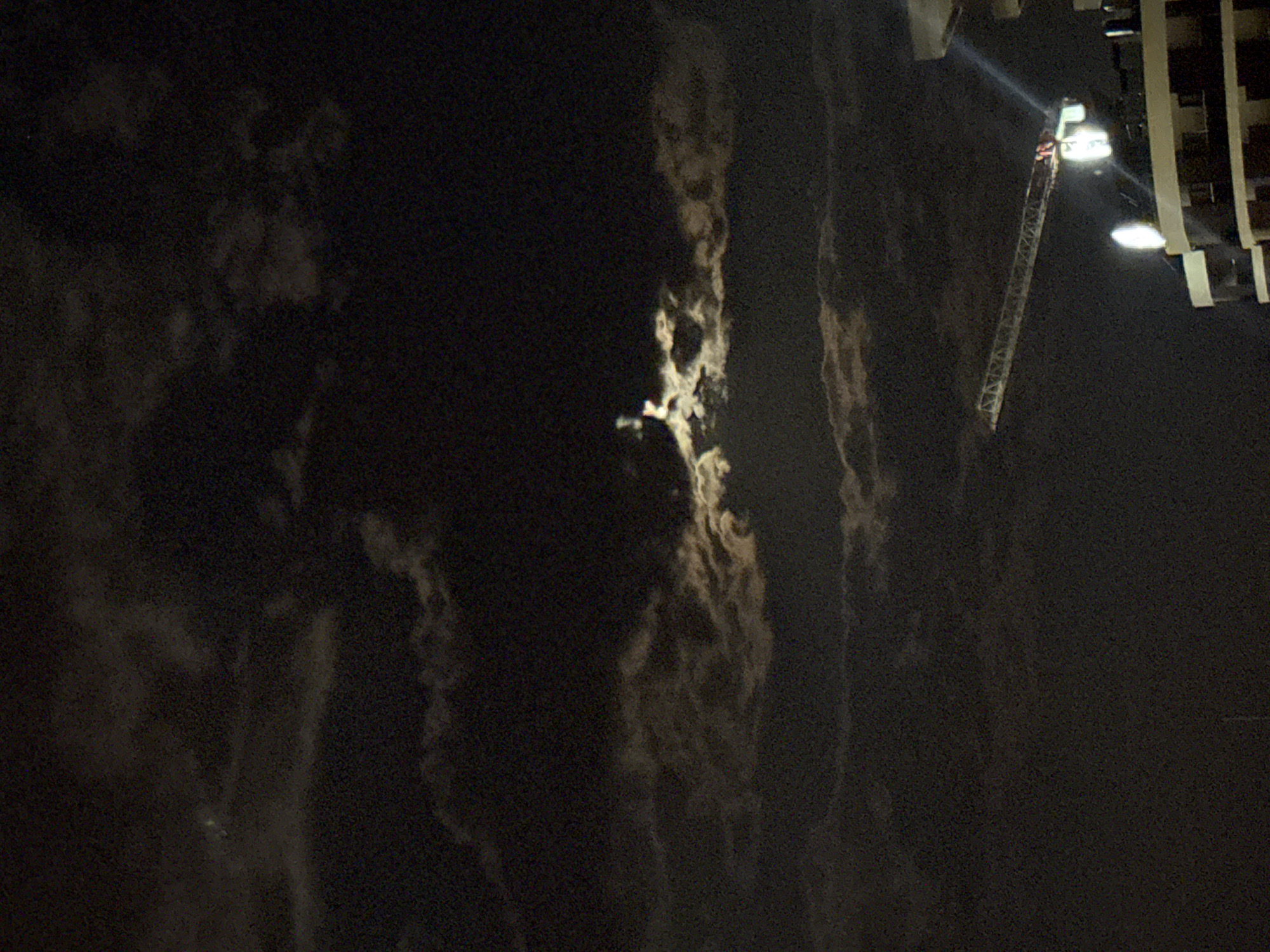 The media file depicts a nighttime rescue operation in Boreti, Montenegro. A fire truck's ladder is extended upwards towards a building, with a spotlight illuminating the scene. A person, likely a firefighter, is visible on the ladder near the top, seemingly engaged in a rescue. The surrounding environment is dark, suggesting it is late at night. The building appears to be multi-story, with some illuminated windows visible on the right side. The sky is dark, with no discernible stars or moon, though some hazy, cloud-like formations are present in the background. The overall mood is one of urgency and action, typical of a rescue scenario. No visible text is present in the image.