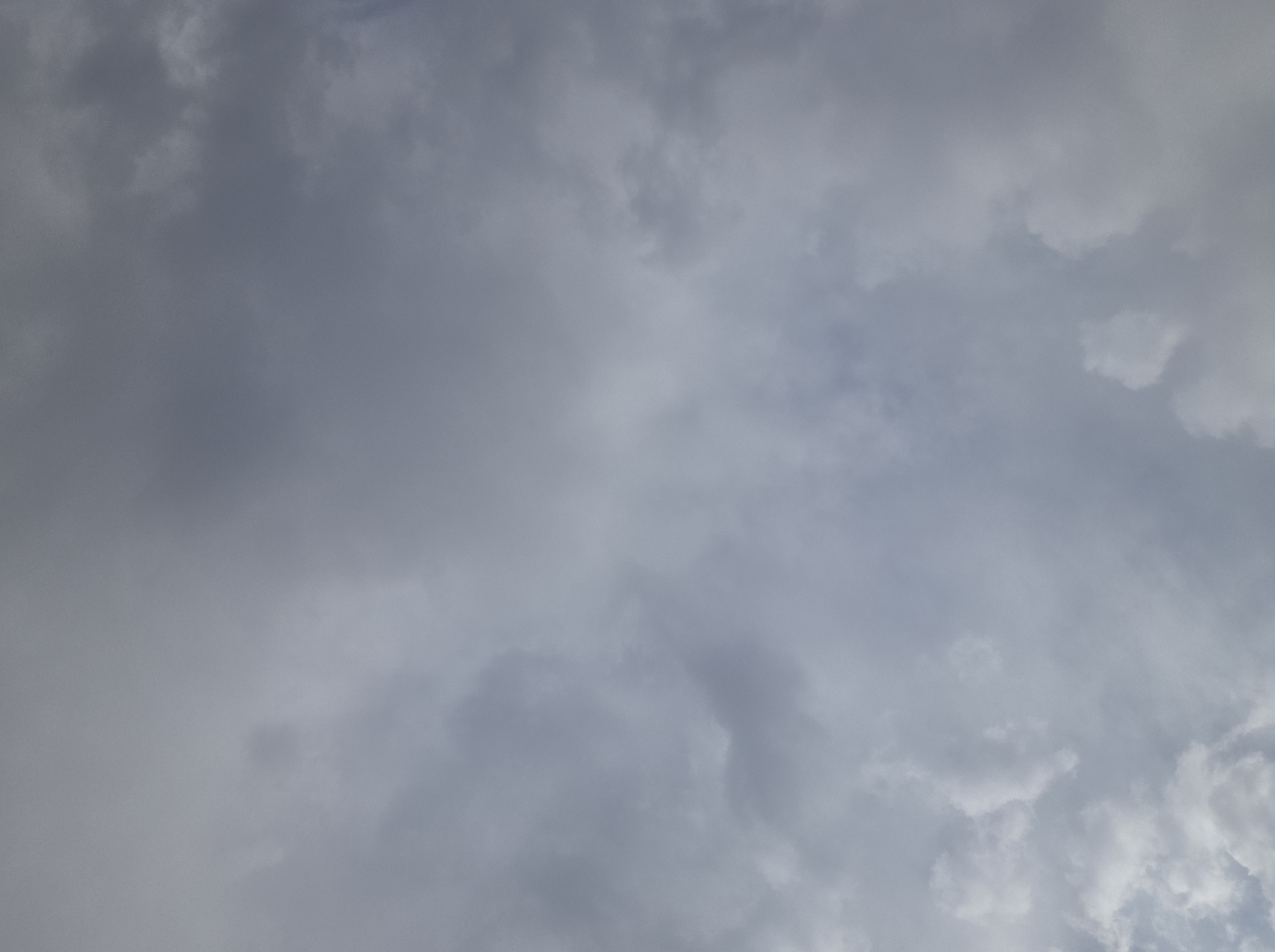 A gray, overcast sky with scattered clouds. The clouds are dense and appear to be composed of moisture, suggesting a cloudy or potentially rainy day. The lighting is diffused, indicating an absence of direct sunlight. The image captures a wide expanse of the sky with no discernible landmarks, buildings, or people. The scene is devoid of any human activity or specific objects. The environment is purely atmospheric, with the focus solely on the cloud formations and the somber sky.